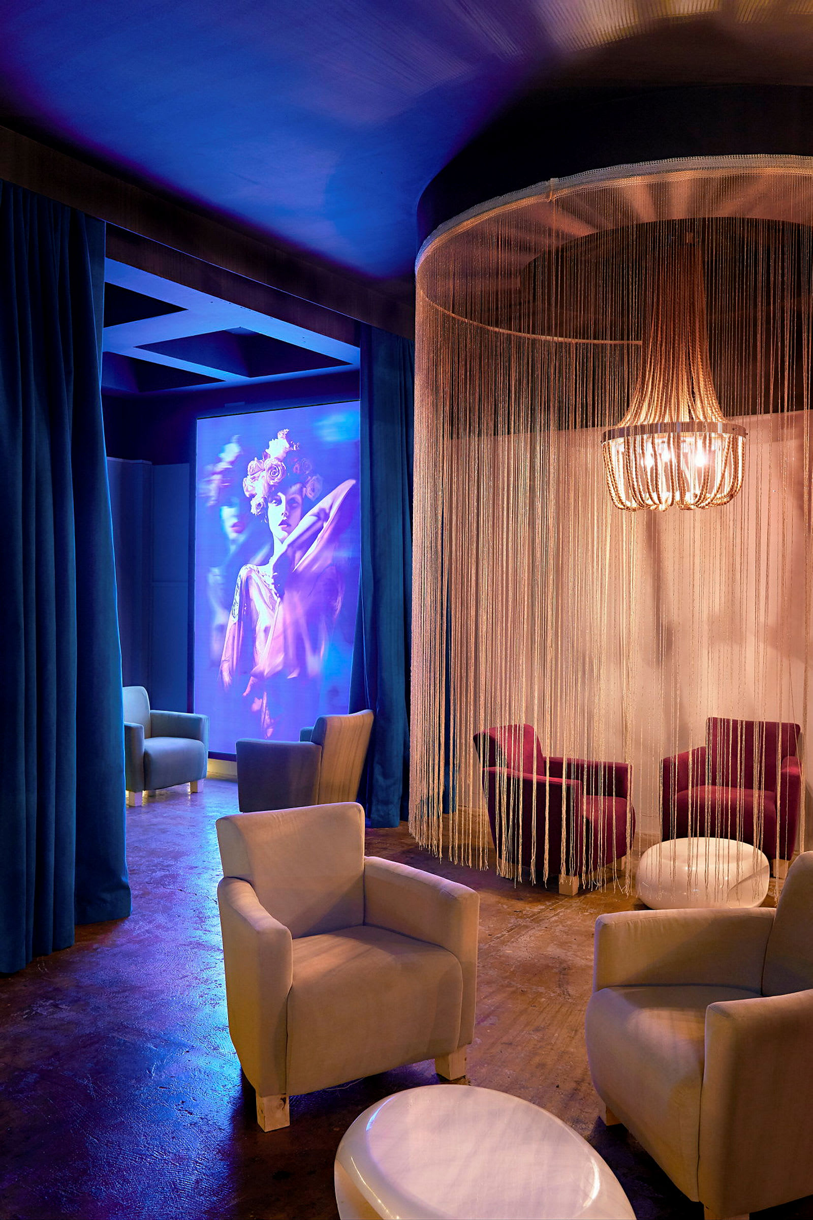 Lounge, jossa nojatuoleja, pöytiä ja koristeellinen lampunvarjostin, valaistu pehmeällä valolla. (Tekoälyn luoma teksti)