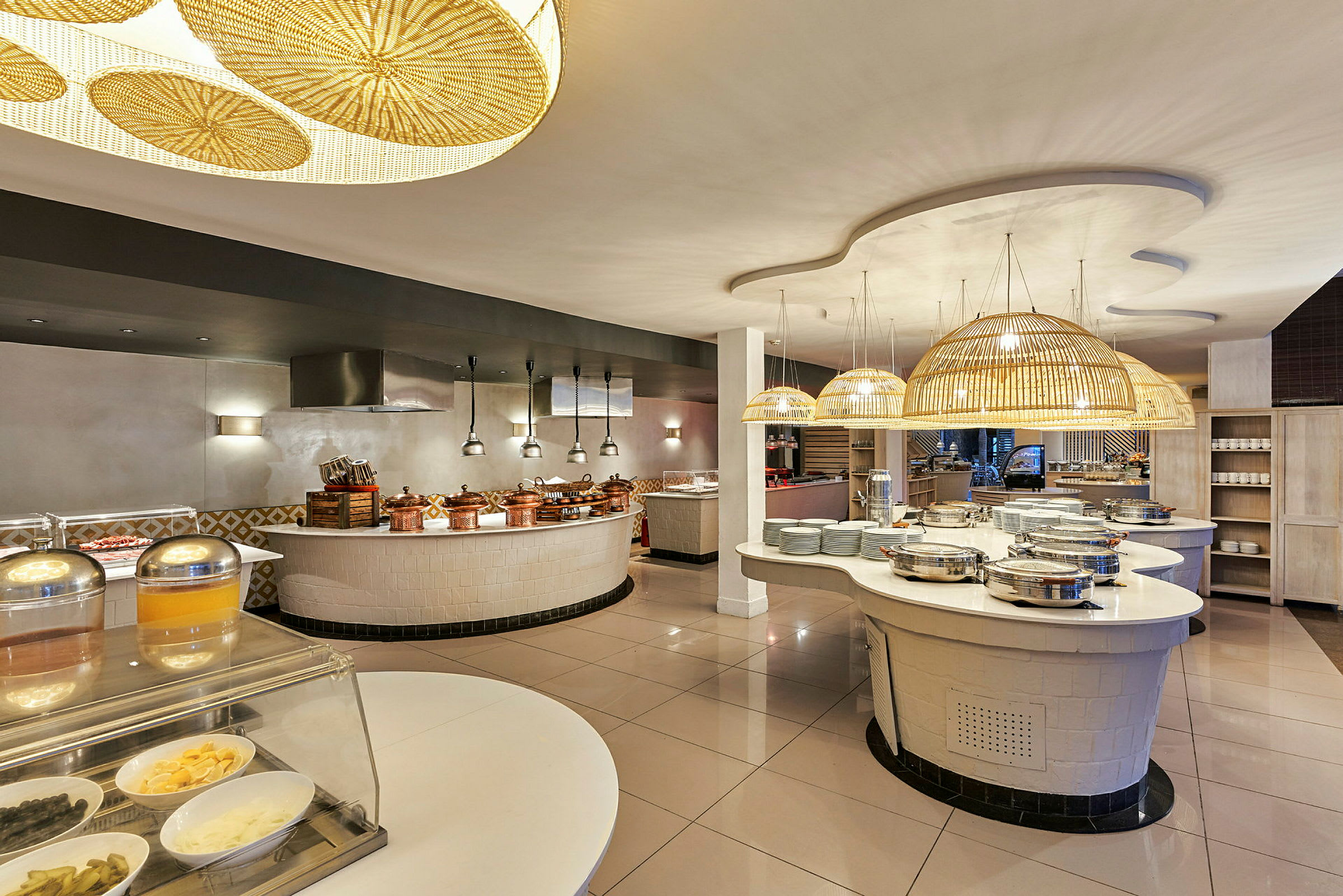 Ravintolan buffet-alue, jossa roikkuvia rottinkilamppuja, tarjoilutiskejä ja ruokasäiliöitä. (Tekoälyn luoma teksti)