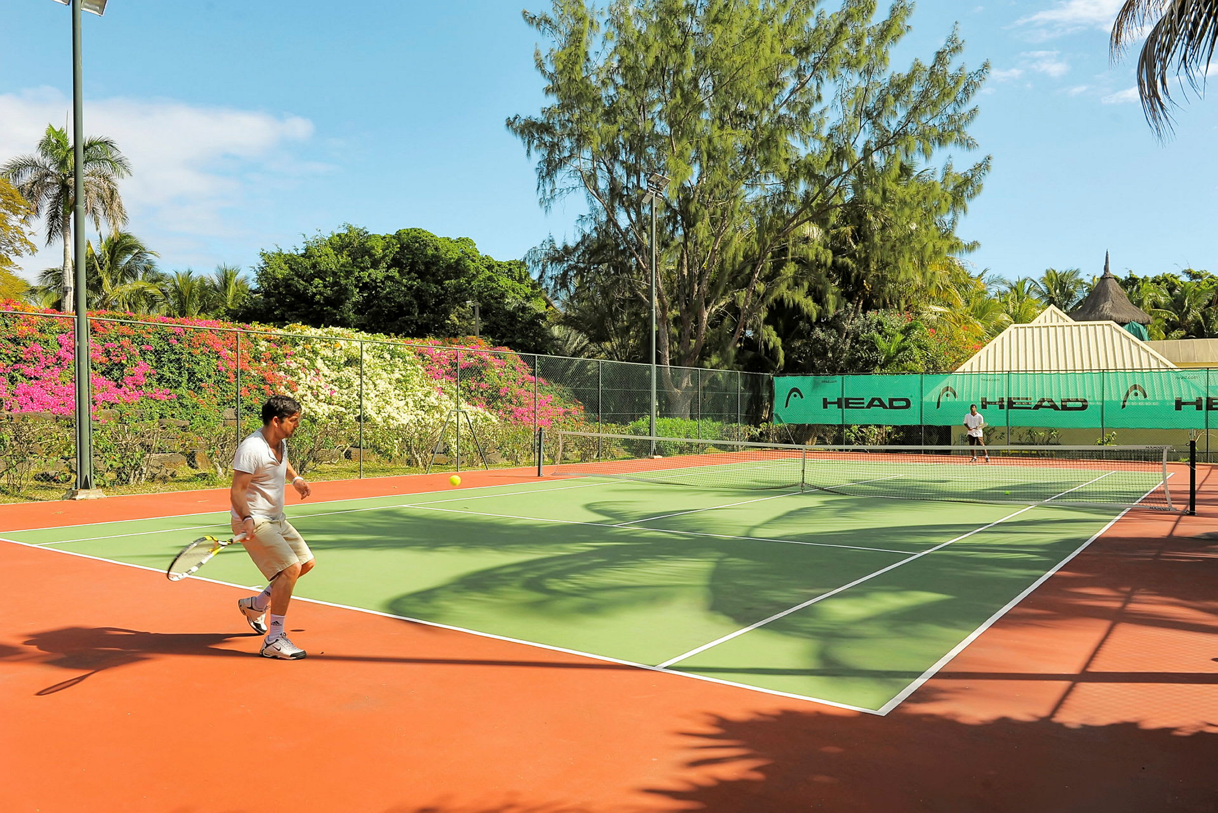 Tenniskenttä vehreyden ja värikkäiden kukkien ympäröimänä. (Tekoälyn luoma teksti)