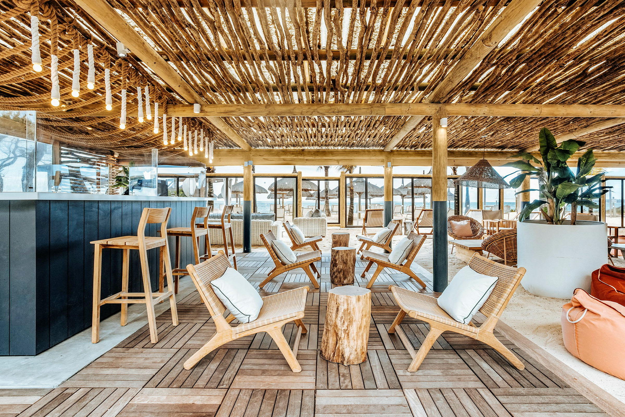 Lounge, jossa on puutuoleja ja pöytiä, sekä katto oksista. (Tekoälyn luoma teksti)