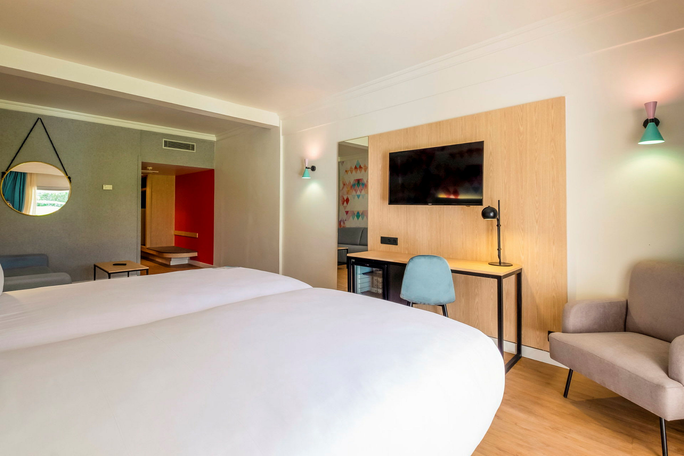 Hotellihuone, jossa parivuode, kirjoituspöytä ja tuoli, televisio sekä istuinpaikka. (Tekoälyn luoma teksti)