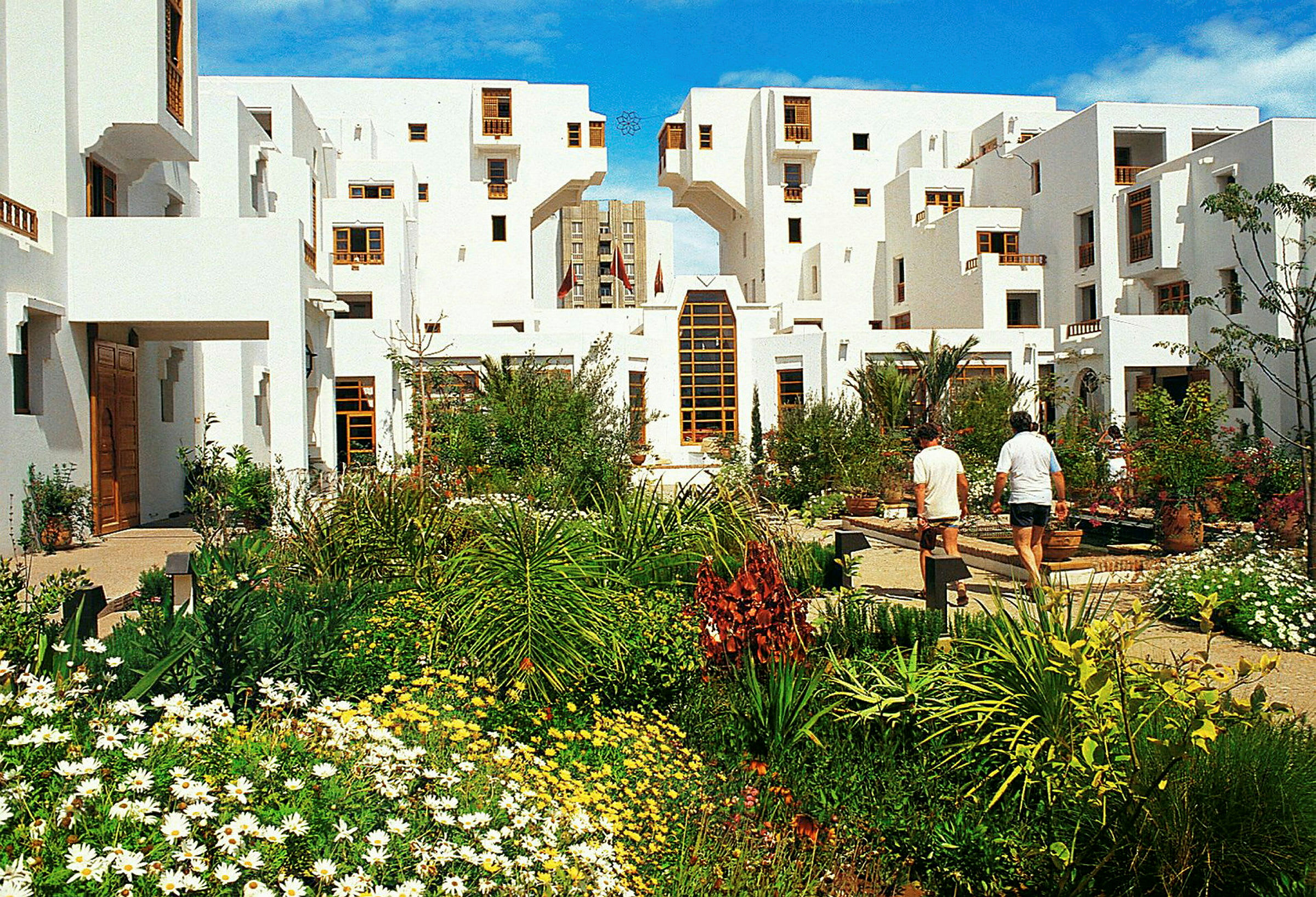 Piha-alue, jossa vehreä puutarha ja valkoisia rakennuksia ikkunoineen ja ovineen. (Tekoälyn luoma teksti)