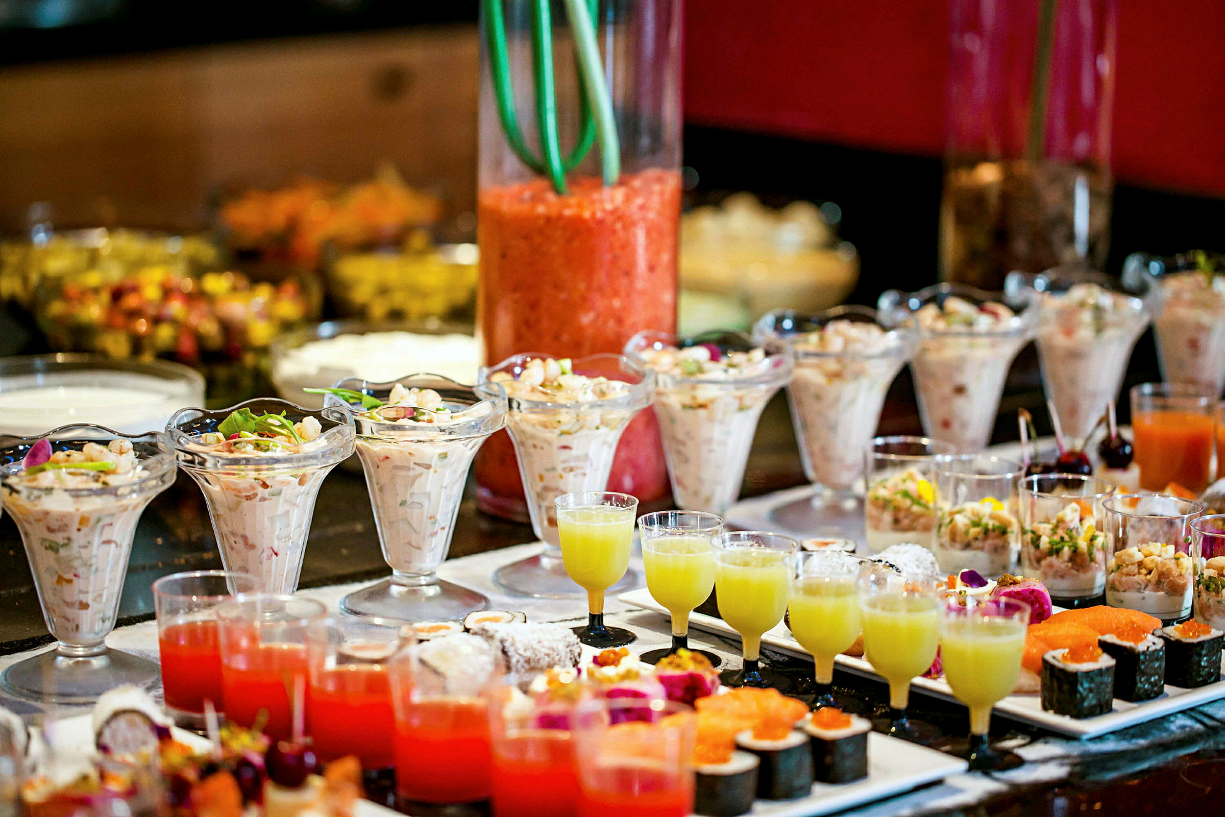 Buffet, jossa on erilaisia ruokalajeja, mukaan lukien pieniä laseja ja kulhoja, jotka sisältävät alkupaloja ja jälkiruokia. (Tekoälyn luoma teksti)