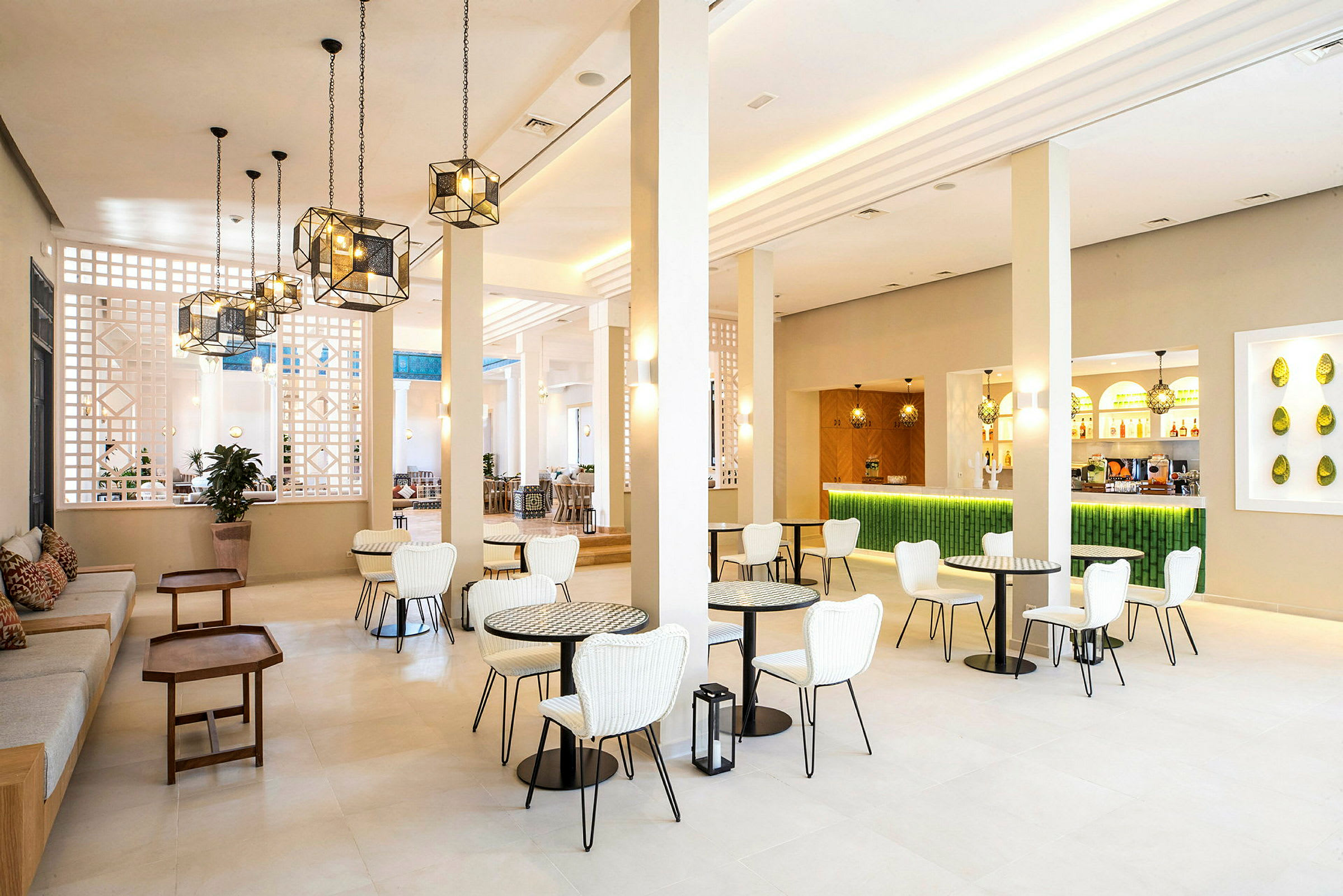 Valkoisilla tuoleilla, pienillä pöydillä ja vihreällä baaritiskillä varustettu valoisa ja moderni lounge. (Tekoälyn luoma teksti)