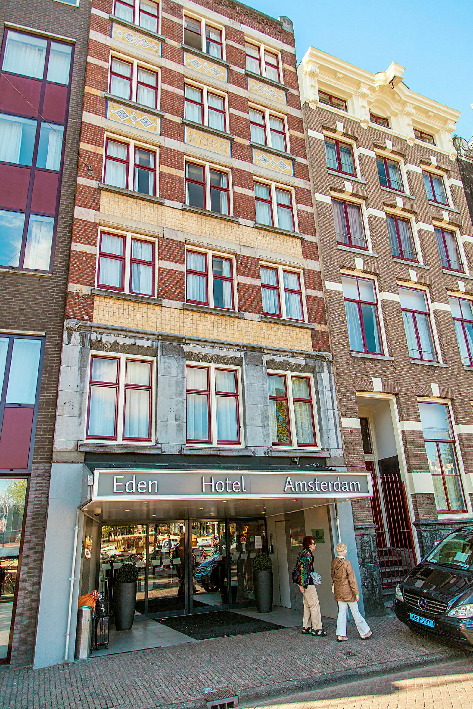 Eden Hotel Amsterdamin etupuoli sisäänkäynnillä ja ihmisiä rakennuksen edessä. (Tekoälyn luoma teksti)