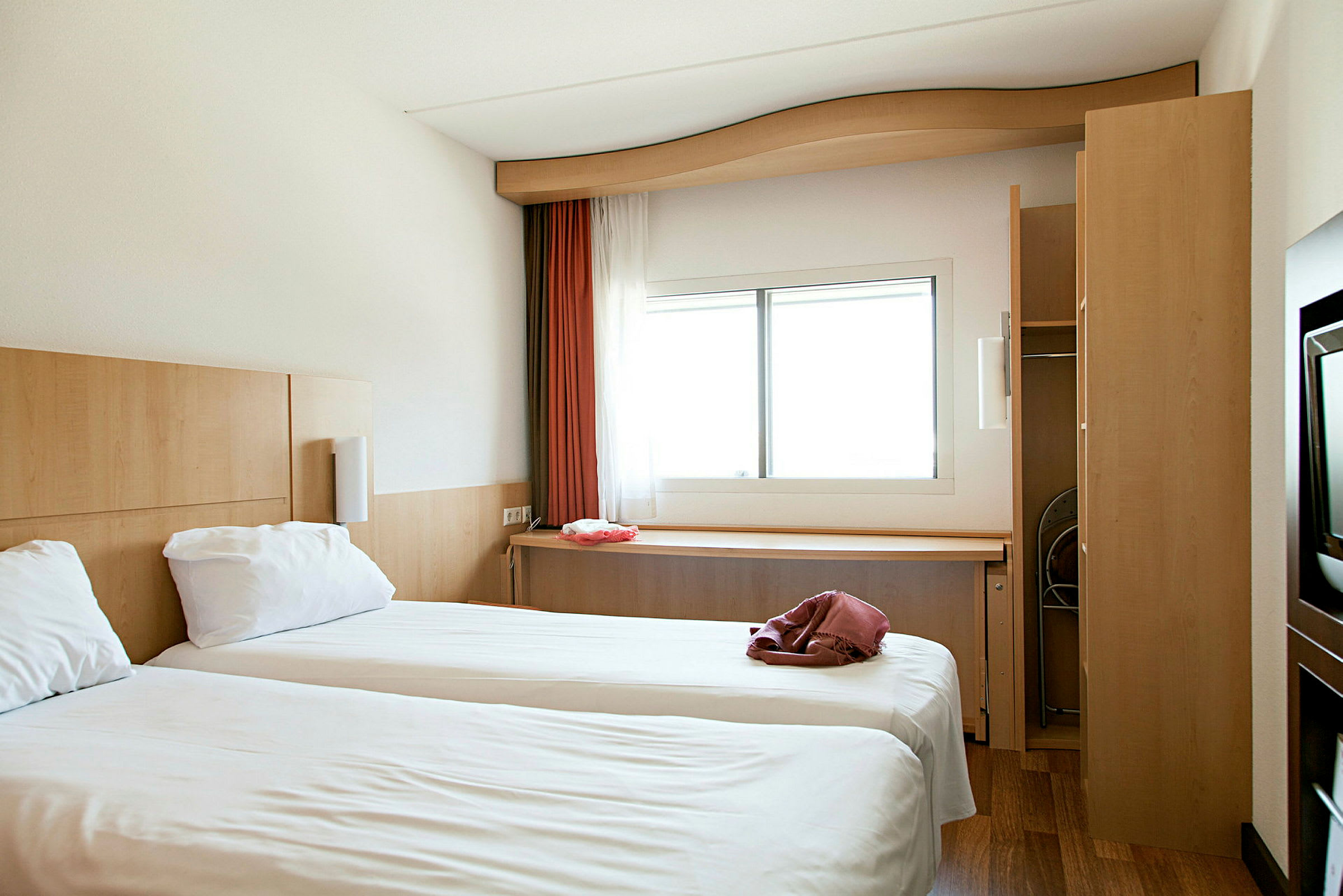 Hotellihuone, jossa kaksi erillistä vuodetta ja ikkuna, josta tulee valoa. (Tekoälyn luoma teksti)