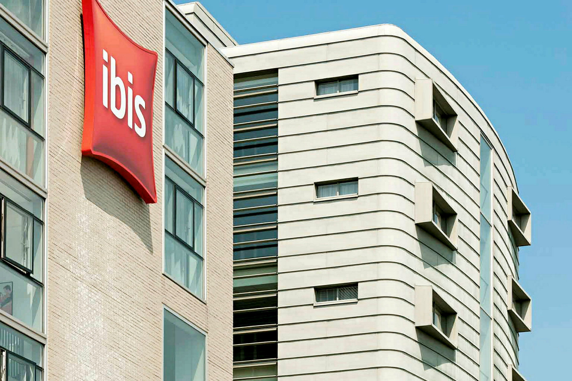 Useita kerroksia nykyaikaisesta rakennuksesta, jossa on selkeä punainen ibis-kyltti. (Tekoälyn luoma teksti)