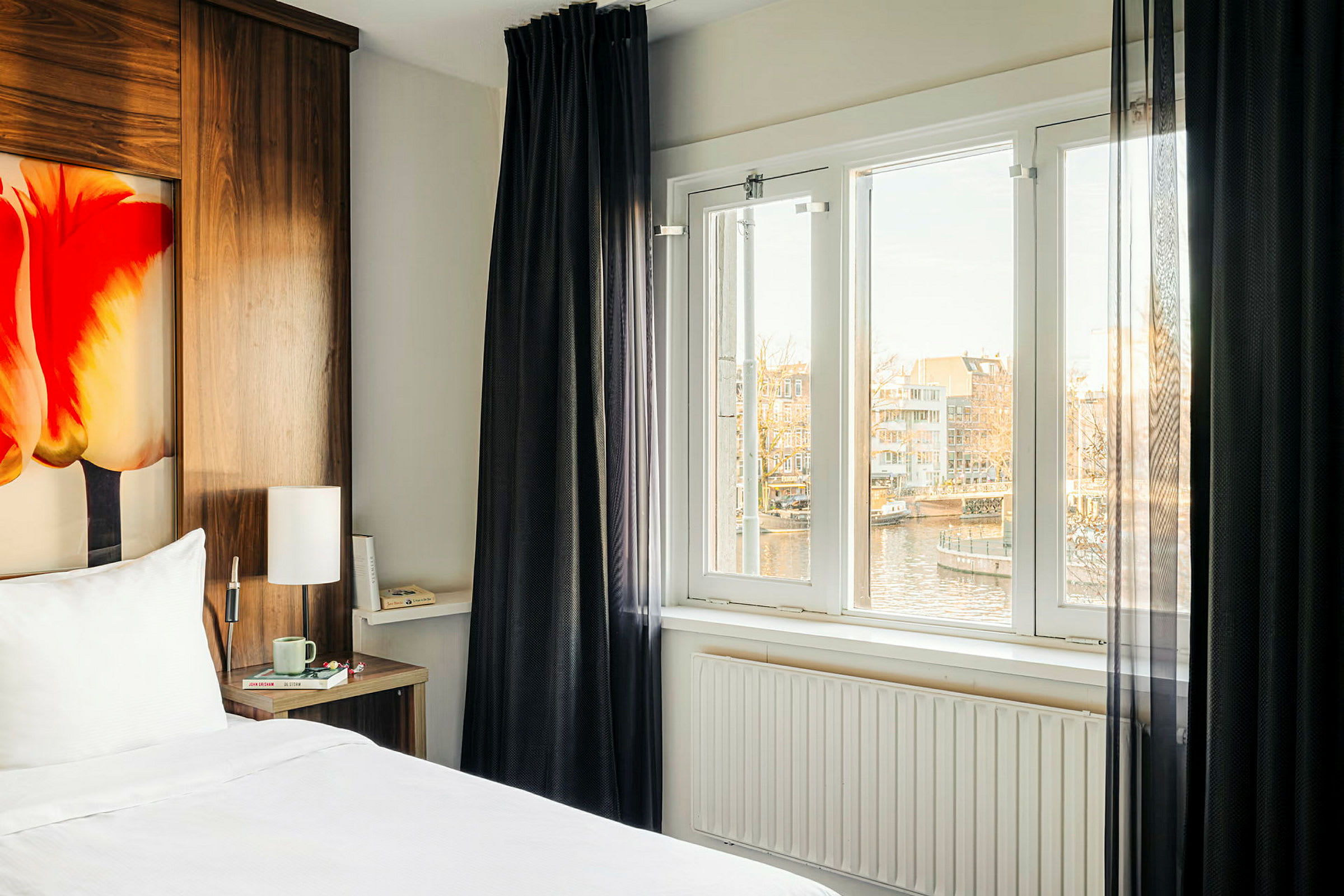 Hotellihuone, jossa on sänky, ikkuna näkymällä kanavalle ja taloihin. (Tekoälyn luoma teksti)