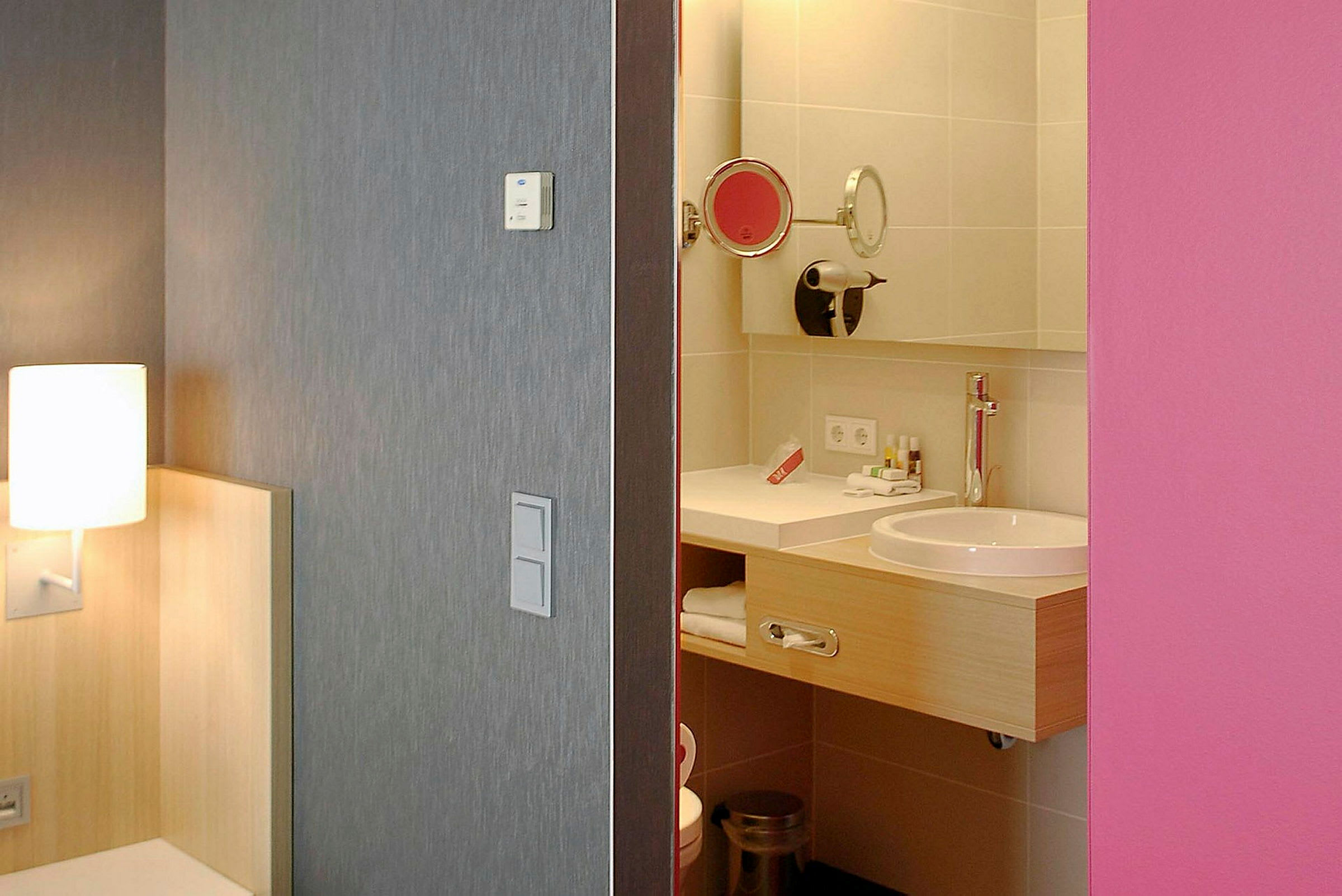 Hotellihuone, jossa näkyy kylpyhuone, lamppu ja sängyn kulma. (Tekoälyn luoma teksti)