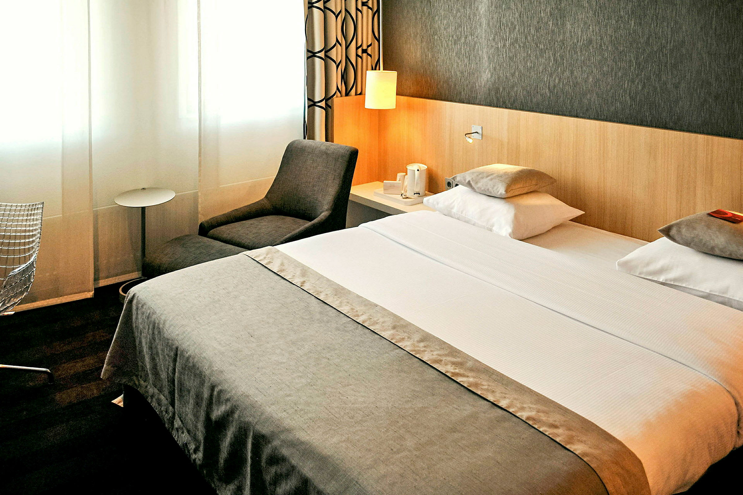 Hotellihuone, jossa parivuode, nojatuoli ja sivupöytä. (Tekoälyn luoma teksti)