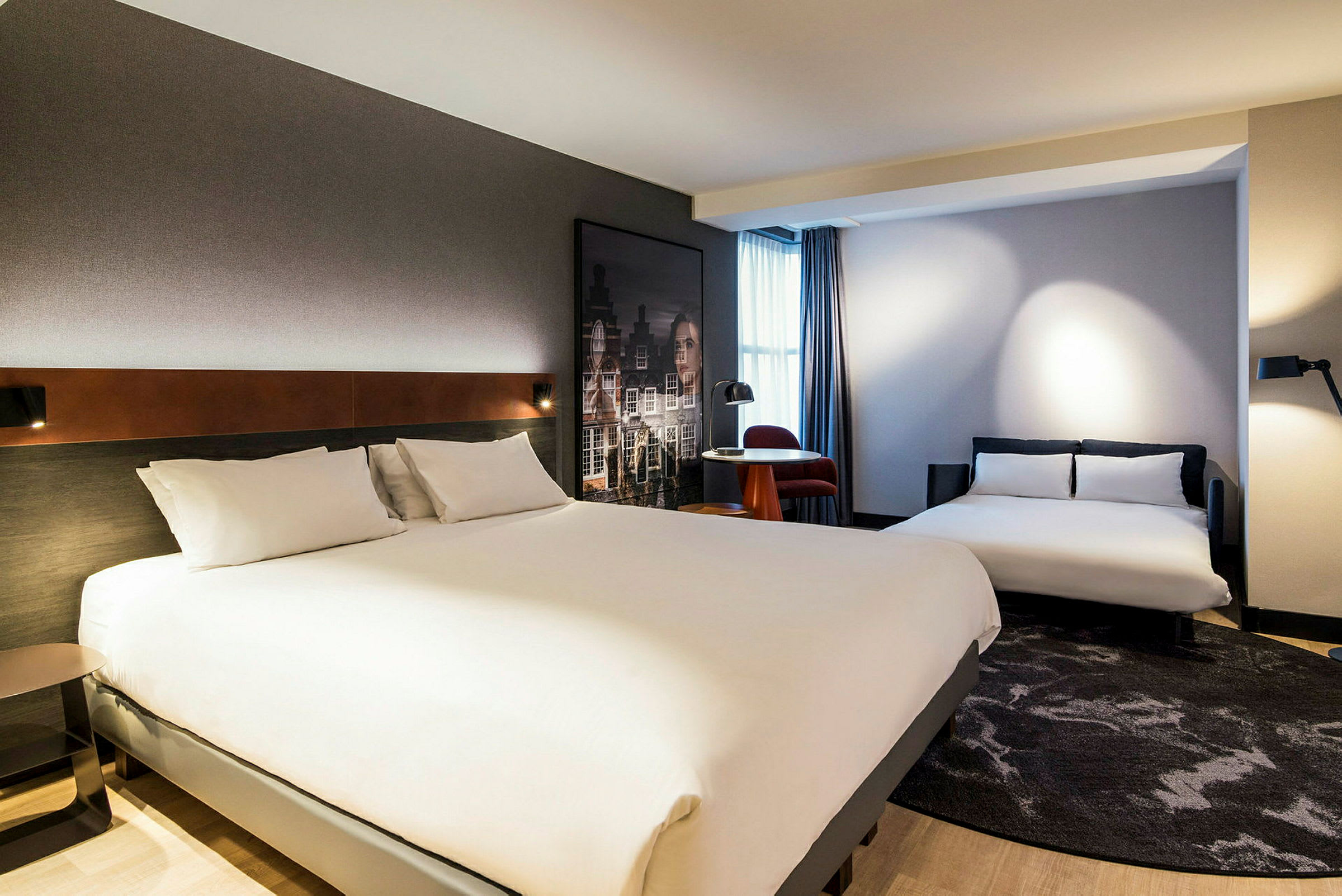 Hotellihuone, jossa on kaksi sänkyä ja pieni pöytä ikkunan lähellä tuolilla. (Tekoälyn luoma teksti)