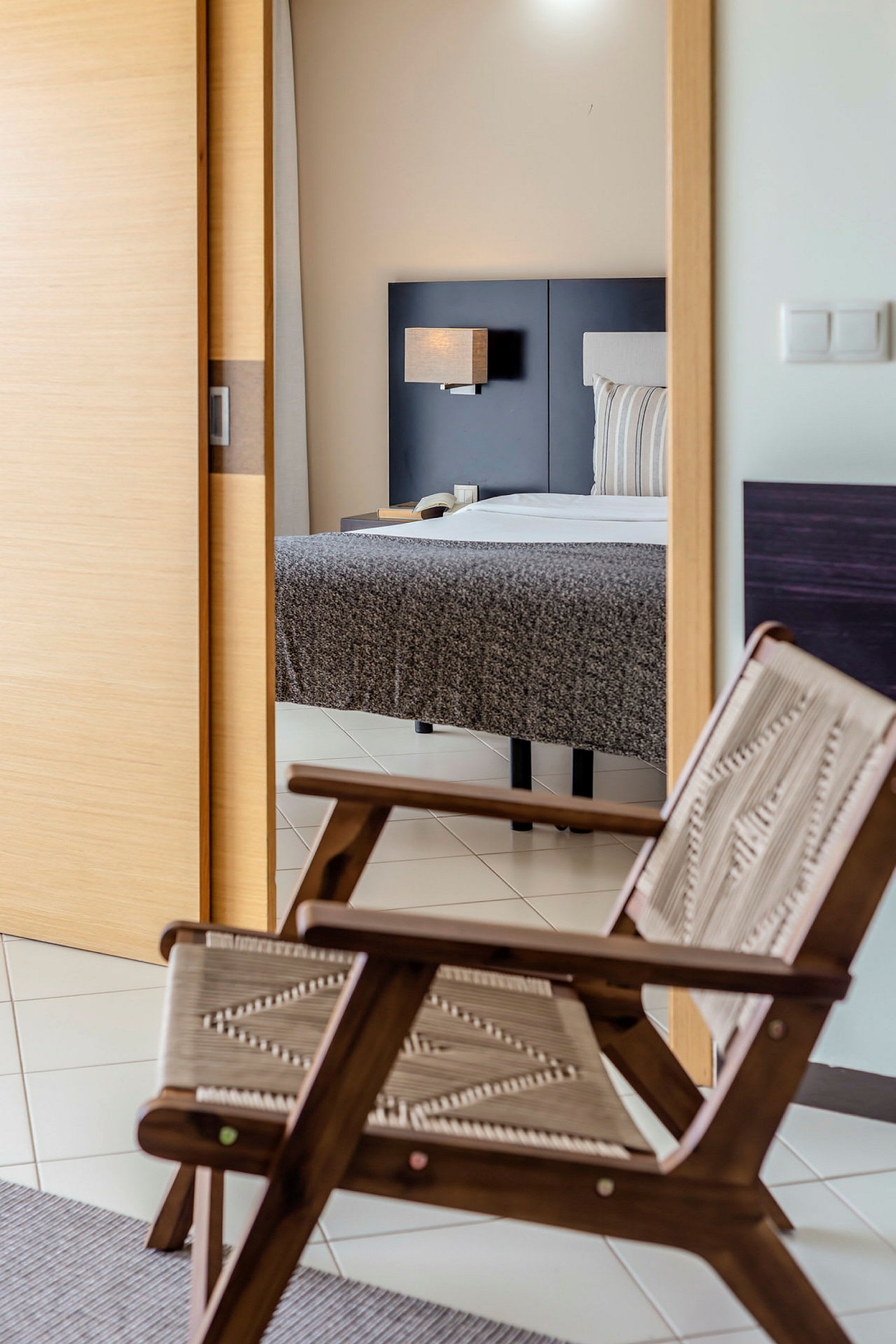 Hotellihuone, jossa tuoli ja sänky taustalla. (Tekoälyn luoma teksti)