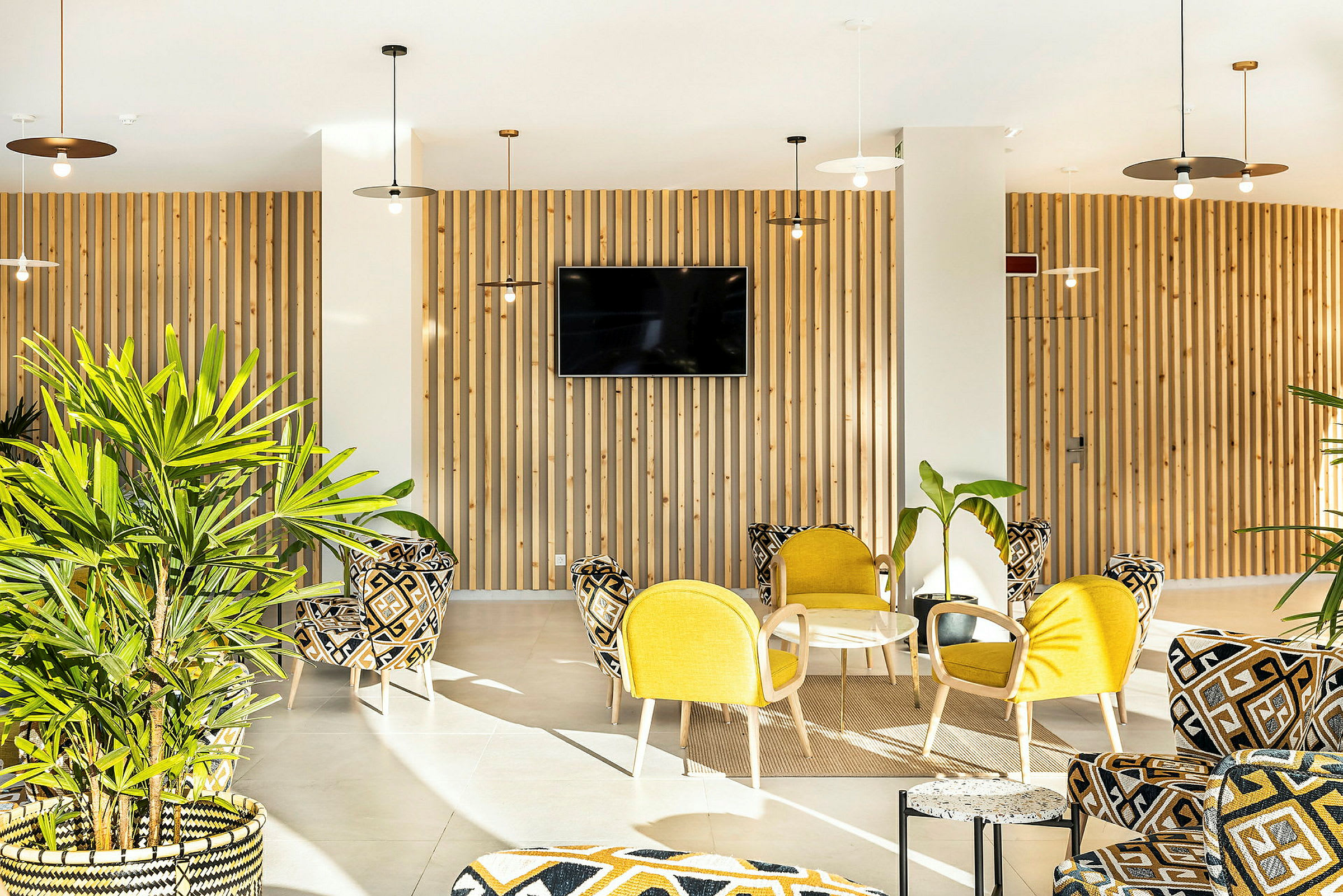 Valoisa ja moderni lounge, jossa on keltaisia ja kuvioituja huonekaluja sekä vihreitä kasveja. (Tekoälyn luoma teksti)