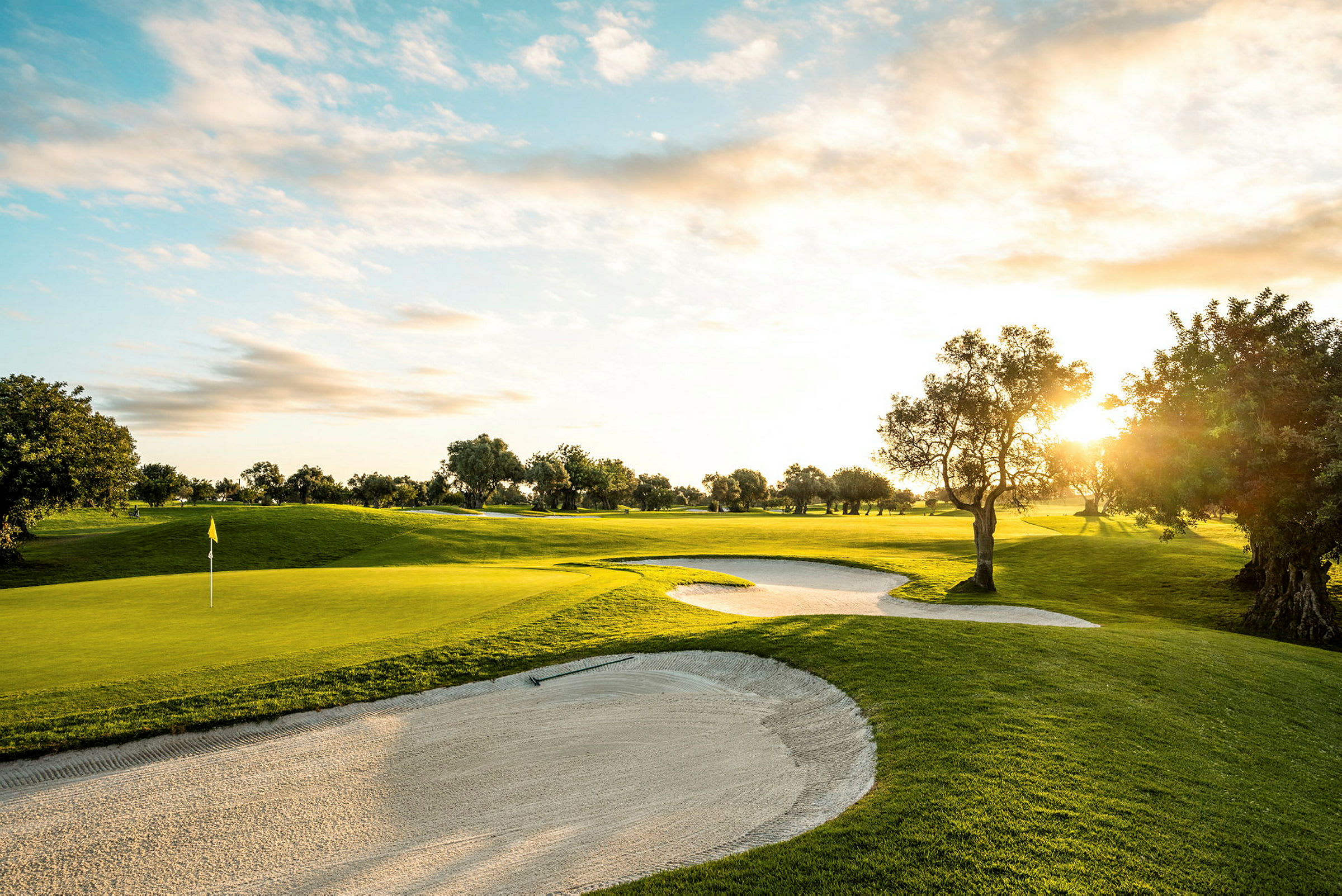 Golfkenttä, jossa hiekkabunkkerit, auringonlasku ja puita. (Tekoälyn luoma teksti)