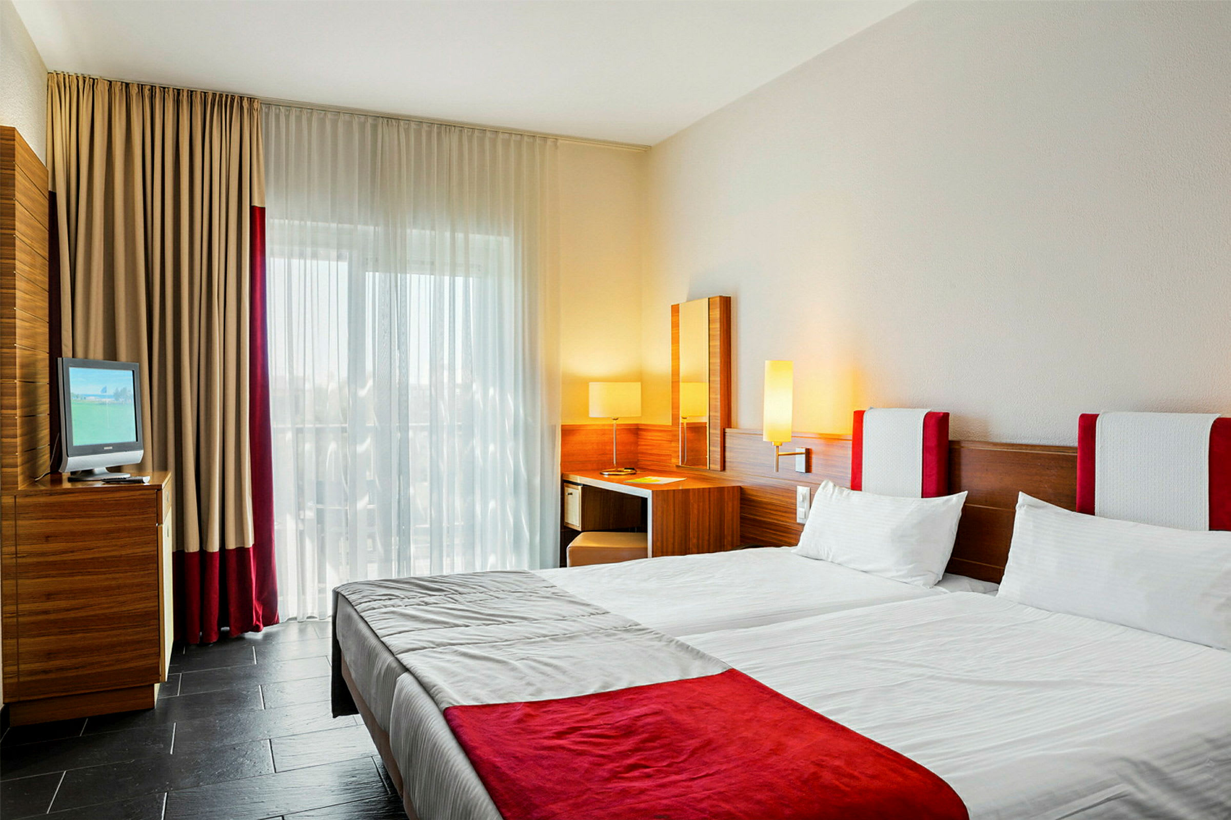 Hotellihuone, jossa kaksi sänkyä, kirjoituspöytä ja verhoilla varustettu ikkuna. (Tekoälyn luoma teksti)