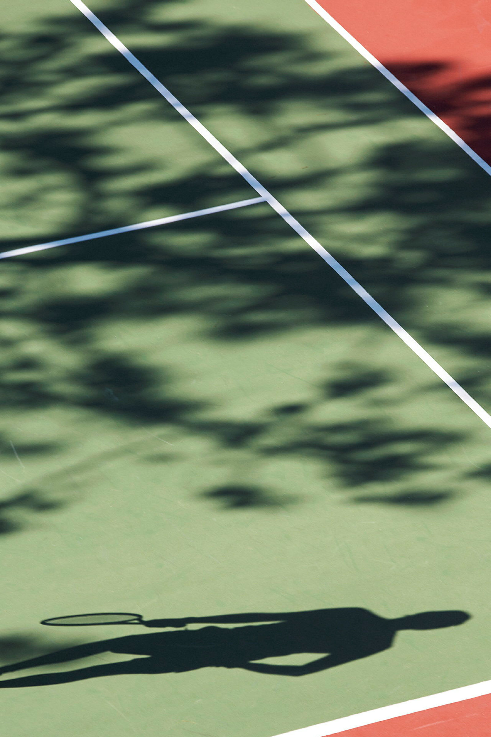 Tenniskentällä olevan henkilön varjo, joka pitää tennismailaa. (Tekoälyn luoma teksti)