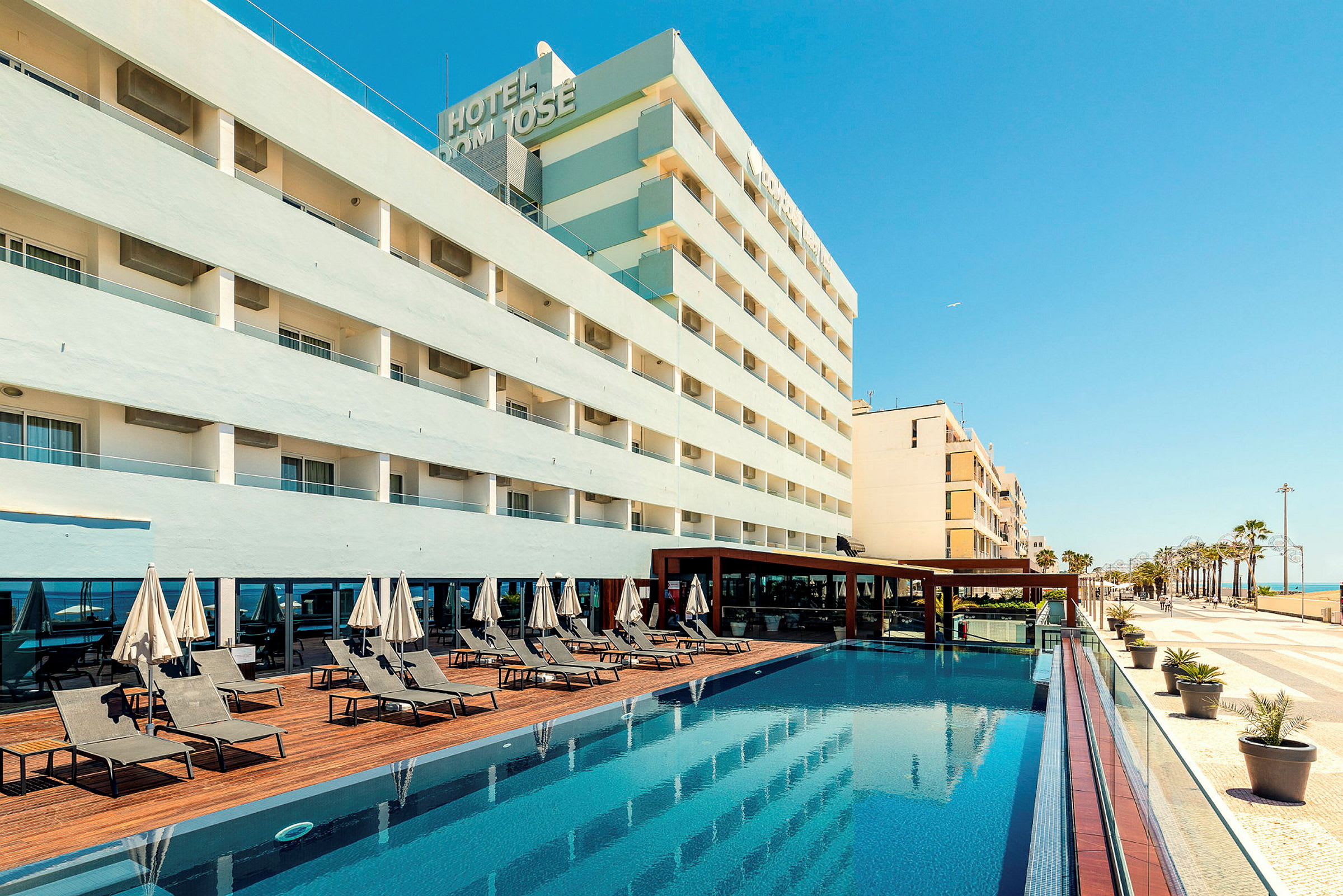 Hotellirakennus, uima-allas ja aurinkotuoleja. (Tekoälyn luoma teksti)