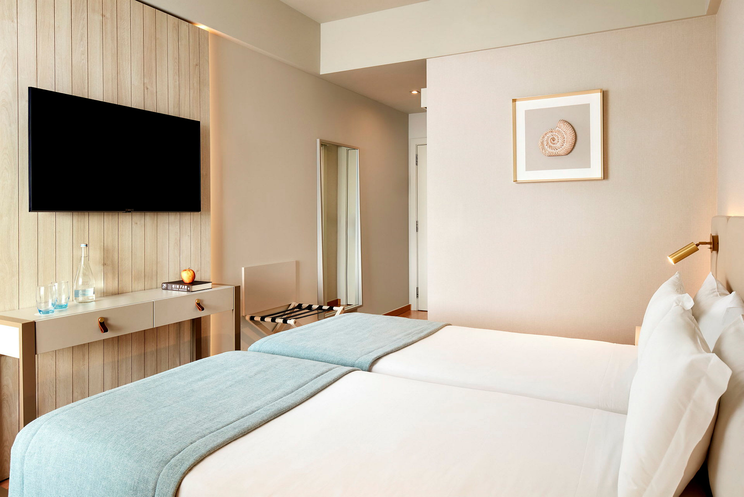 Hotellihuone kahdella erillisvuoteella, seinälle asennettu televisio ja minimalistinen sisustus. (Tekoälyn luoma teksti)