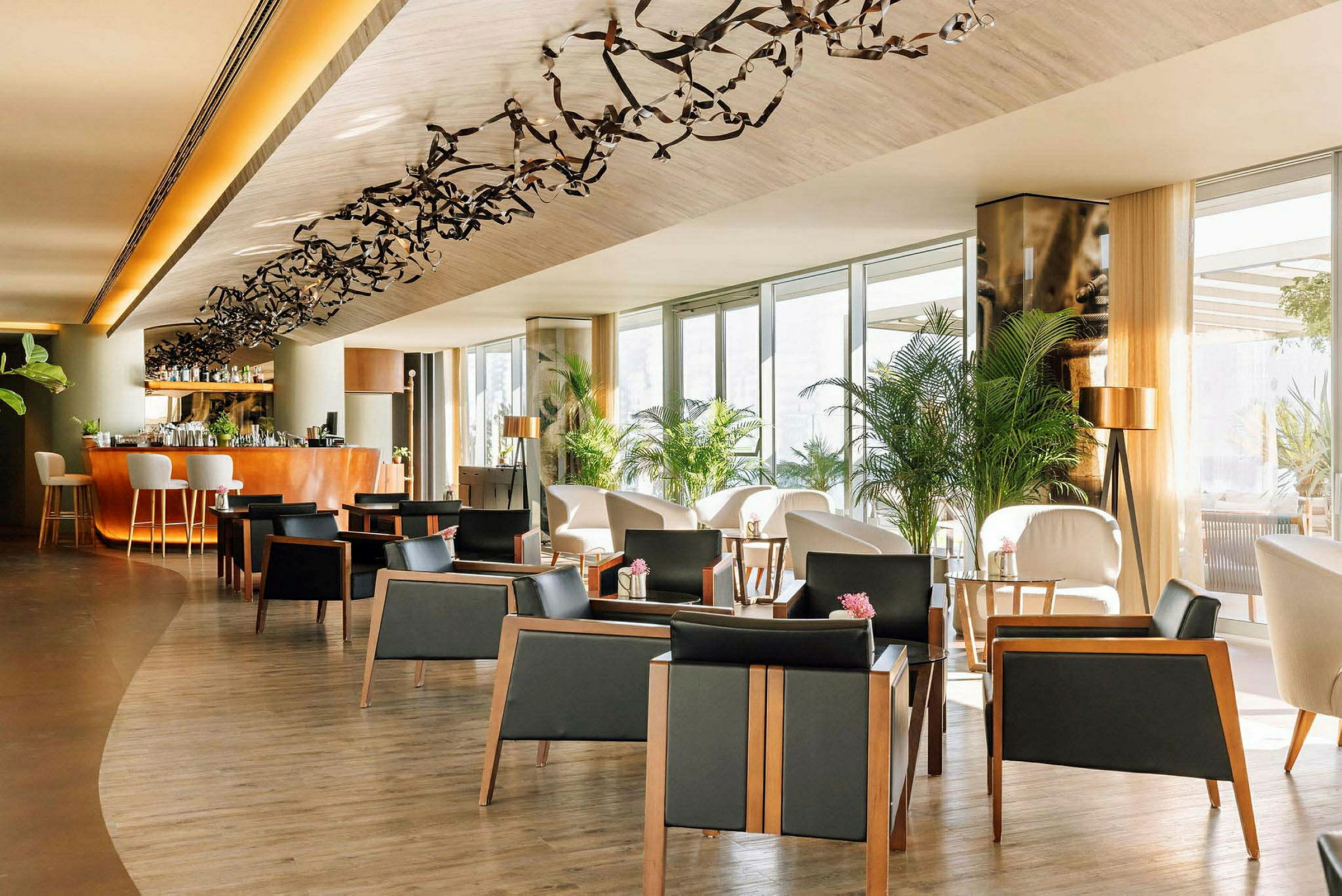 Tyylikäs lounge-alue, jossa on tuoleja, pöytiä ja koristekasveja. Baaritiski taustalla. (Tekoälyn luoma teksti)