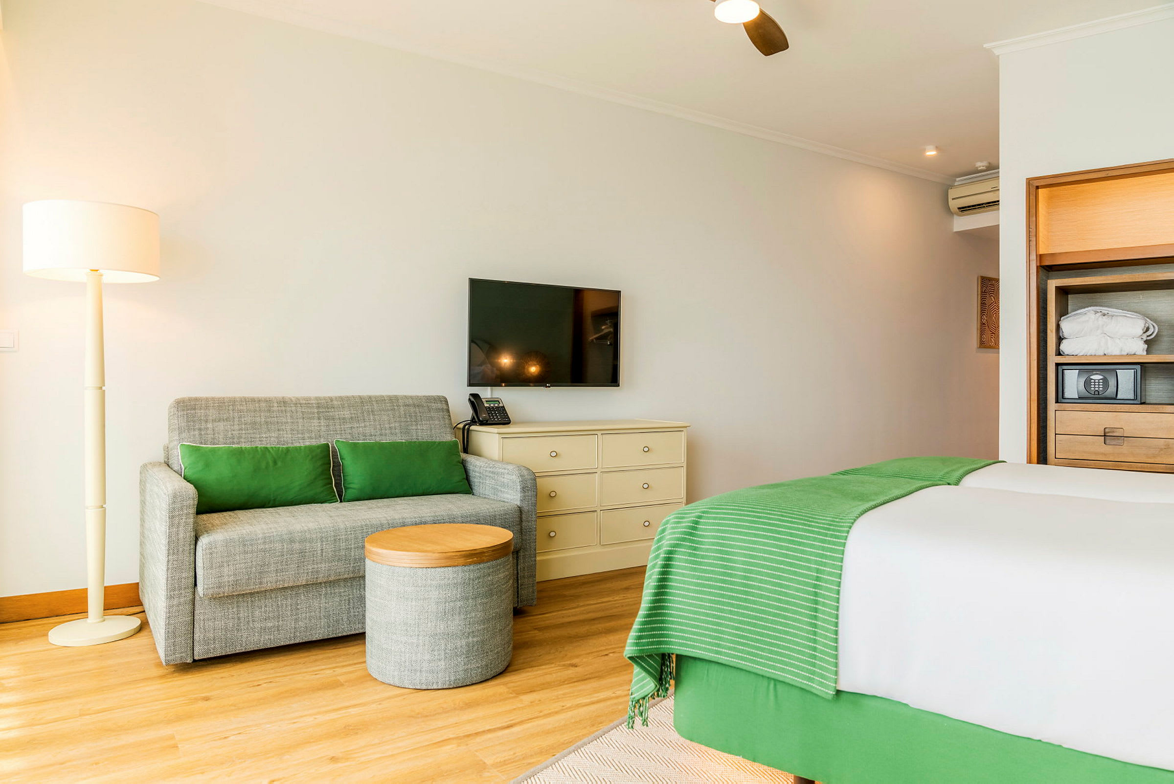 Hotellihuone, jossa on sohva, pieni pöytä, sänky ja seinällä televisio. (Tekoälyn luoma teksti)