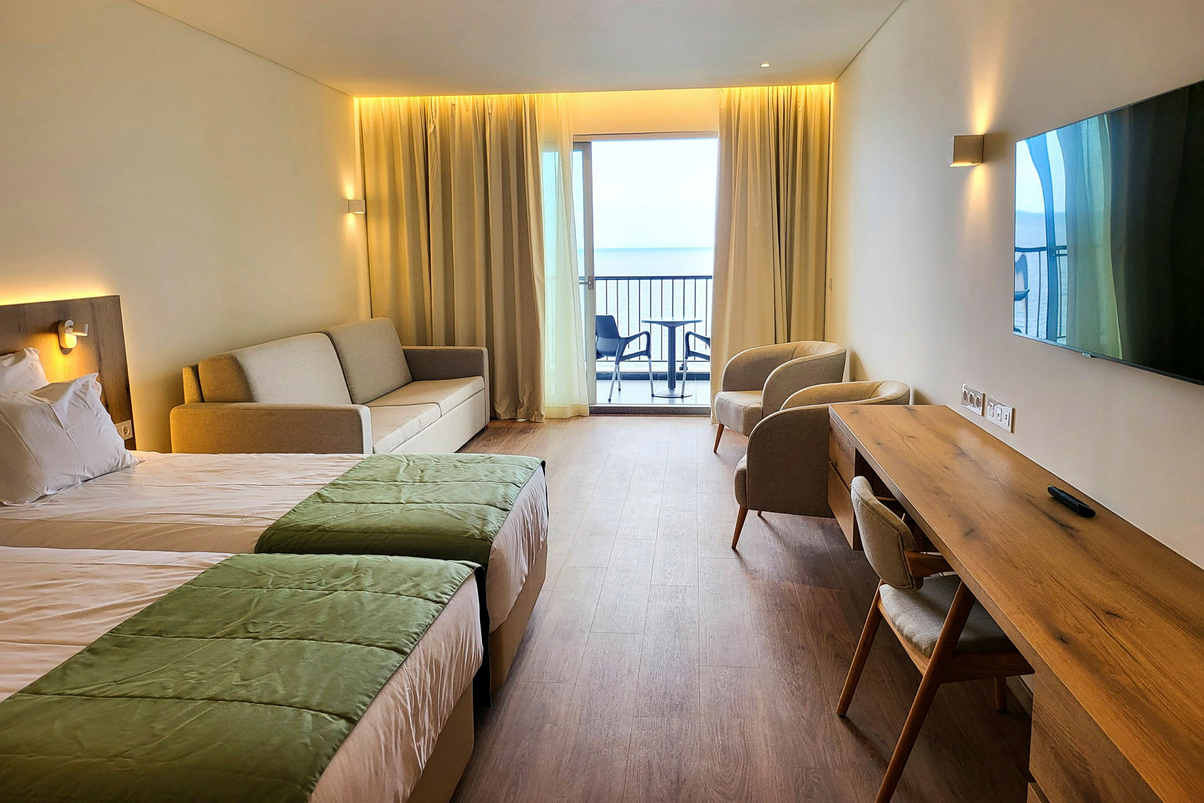 Hotellihuone, jossa kaksi sänkyä, sohva, kaksi nojatuolia, kirjoituspöytä ja parveke näkymällä. (Tekoälyn luoma teksti)