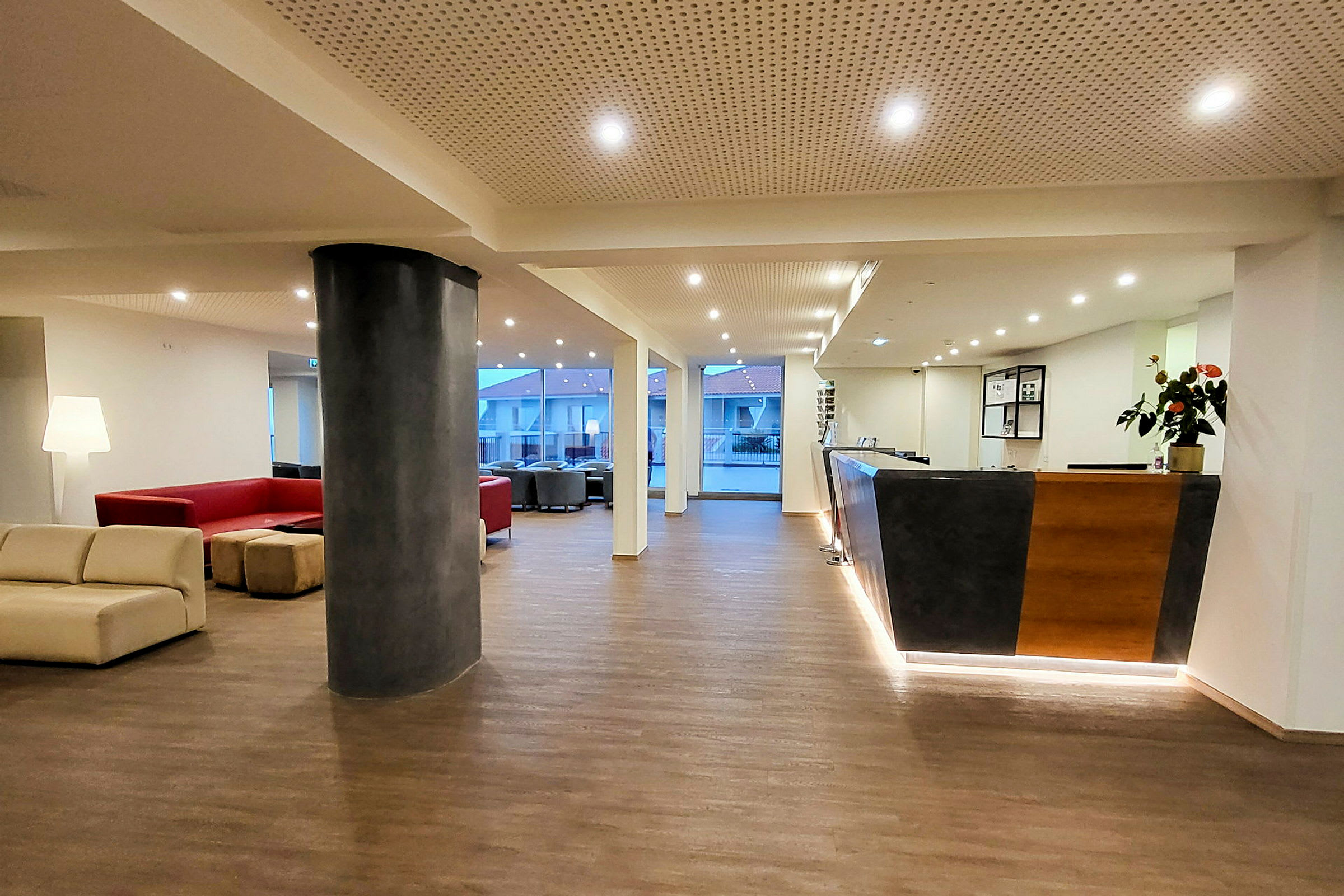 Hotellin aula, jossa istuinryhmiä, vastaanotto ja suuret ikkunat. (Tekoälyn luoma teksti)