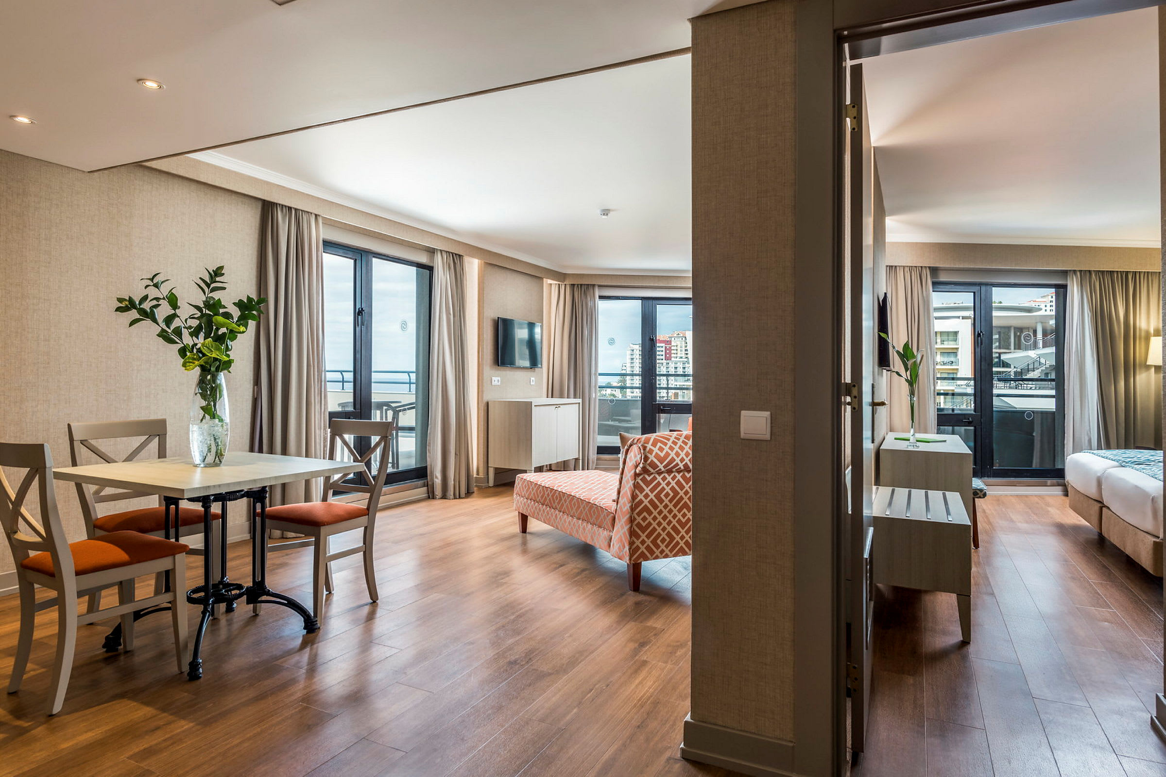 Hotellihuone, jossa olohuone sisältyy ruokapöytä ja tuolit, sekä taustalla näkyvä makuuhuone. (Tekoälyn luoma teksti)
