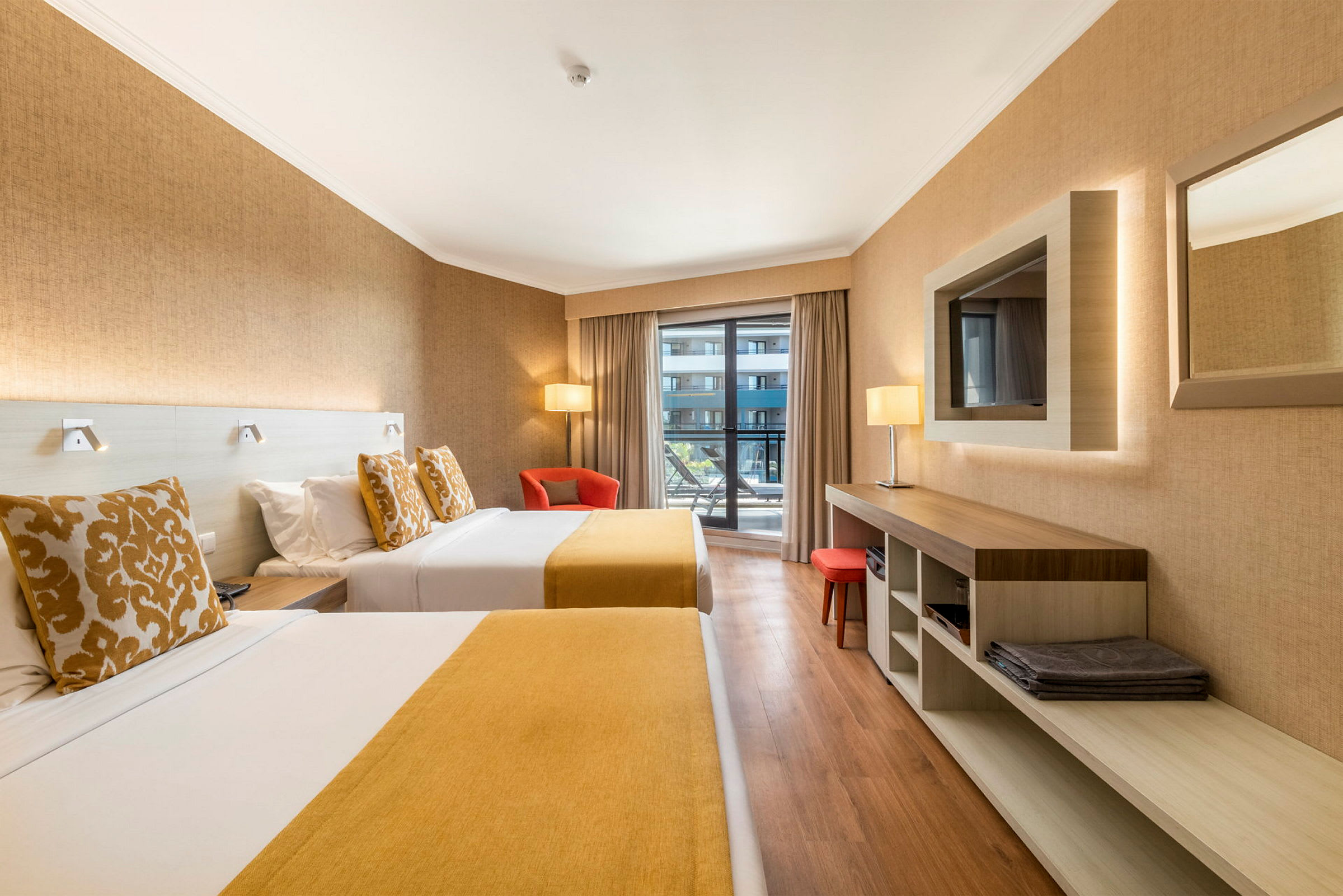 Hotellihuone, jossa on kaksi sänkyä, nojatuoli ja näkymä parvekkeelle. (Tekoälyn luoma teksti)