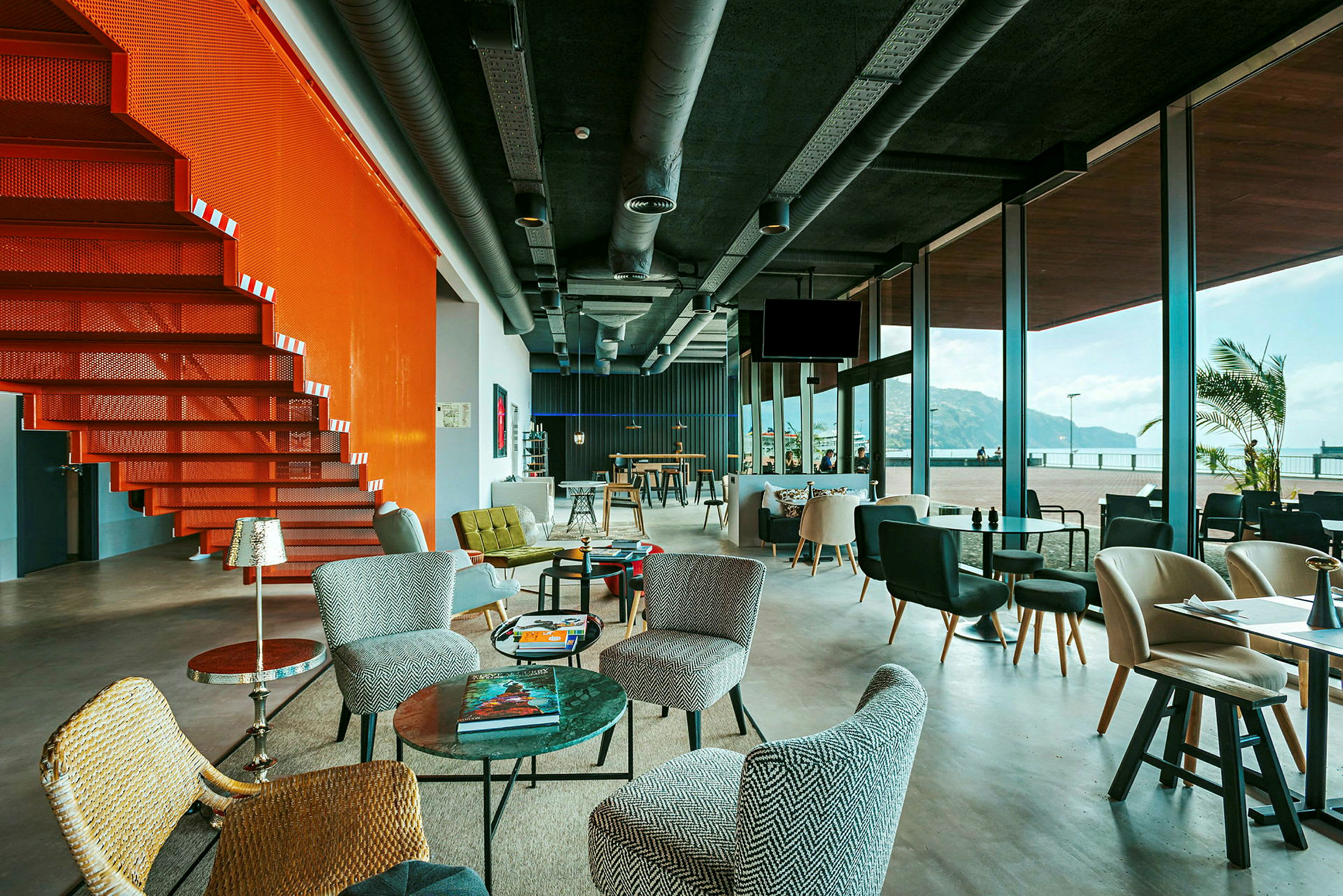 Moderni lounge, jossa on suuret lasi-ikkunat ja oranssi porraskäytävä. (Tekoälyn luoma teksti)
