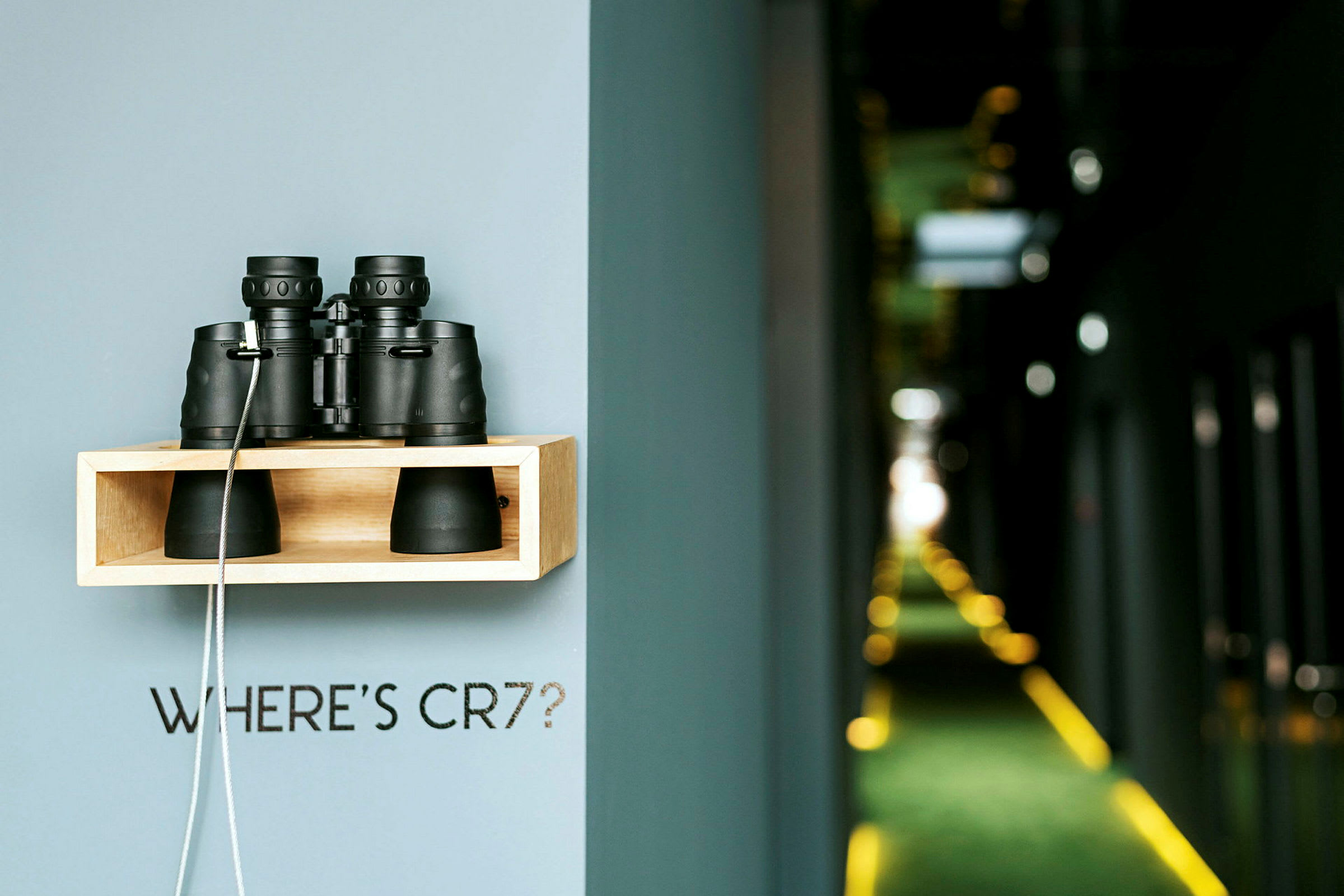 Hylly, joka on kiinnitetty seinään ja jonka päällä on kiikari, ja teksti "WHERE'S CR7?", taustalla sumuinen käytävä. (Tekoälyn luoma teksti)