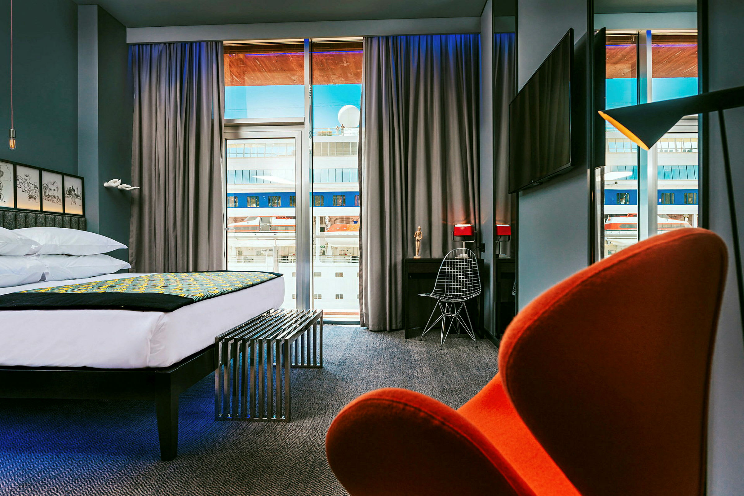 Moderni hotellihuone, jossa on iso sänky, kirjoituspöytä ja tuoli sekä näkymä suurista ikkunoista. (Tekoälyn luoma teksti)