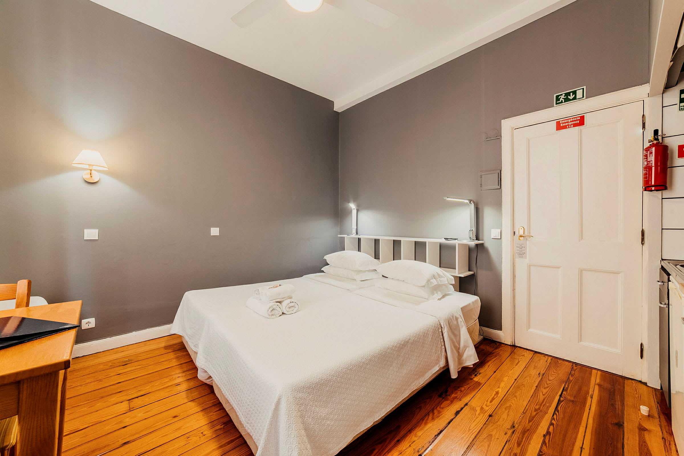Hotellihuone, jossa on harmaat seinät, puulattia ja parisänky. (Tekoälyn luoma teksti)