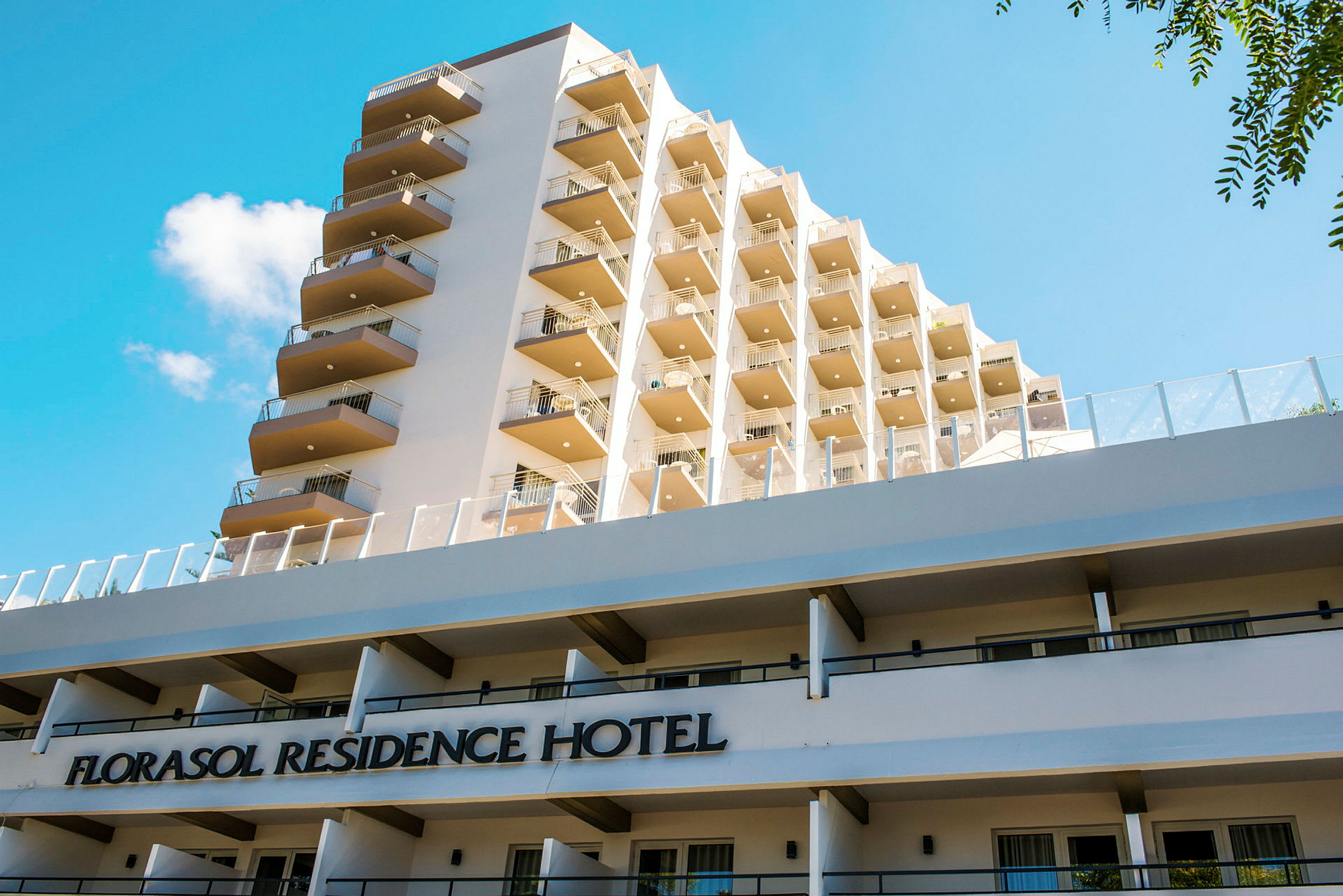 Näkymä Florasol Residence Hotel -rakennuksesta, jossa on useita parvekkeita ja sininen taivas taustalla. (Tekoälyn luoma teksti)