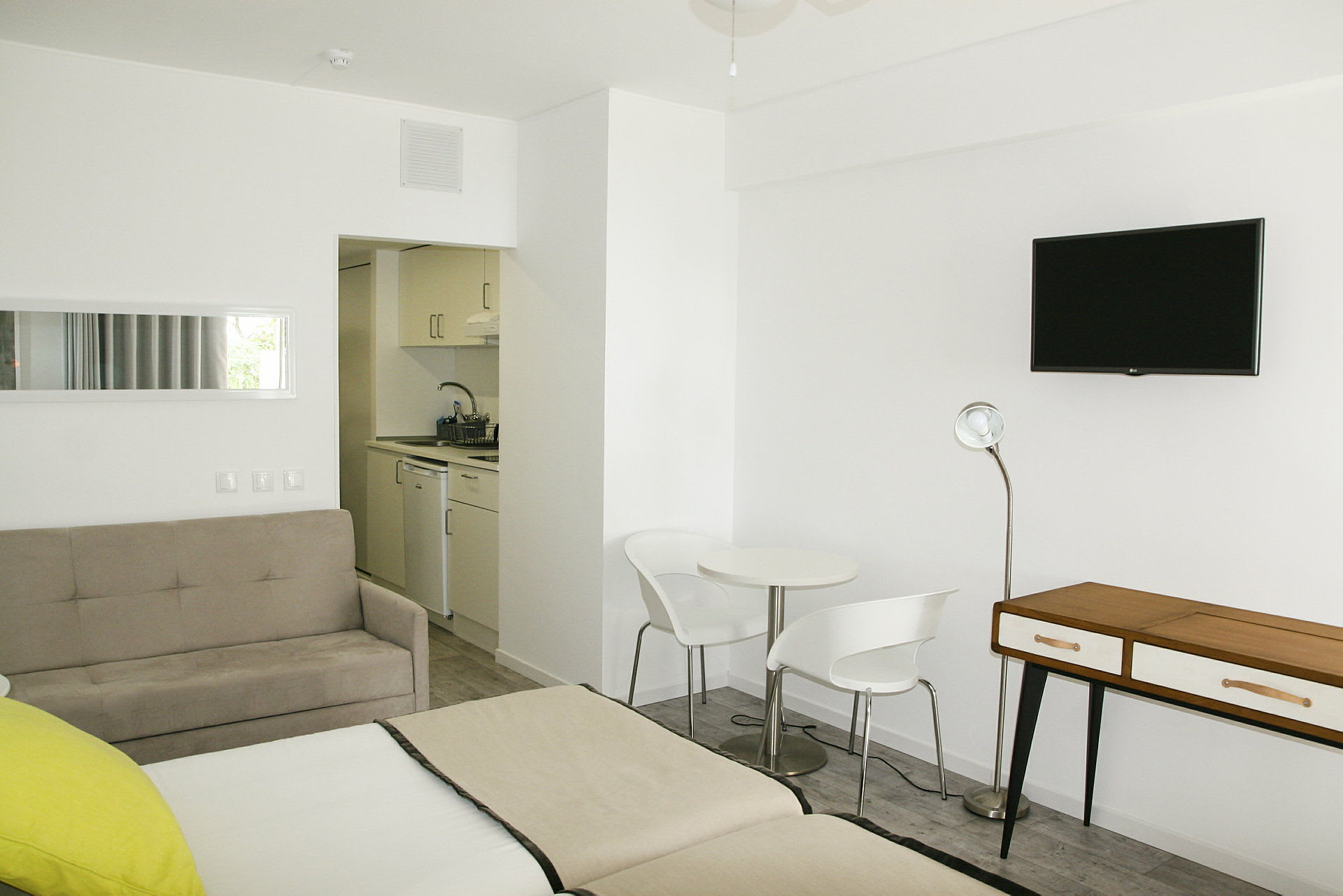 Moderni hotellihuone, jossa on valkoiset seinät, istuinryhmä ja pieni keittiö. (Tekoälyn luoma teksti)