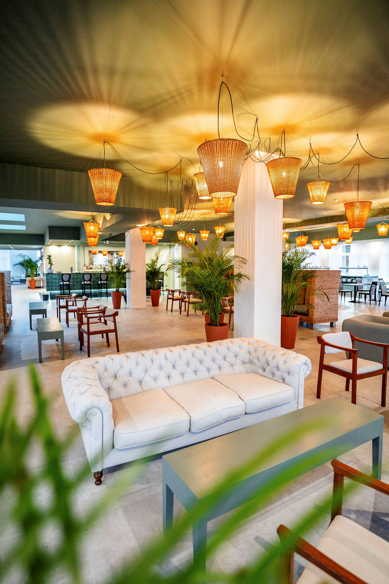 Tyylikäs lounge, jossa valkoinen sohva, puuhuonekaluja, vihreitä kasveja ja rottinkikattovalaisimia. (Tekoälyn luoma teksti)