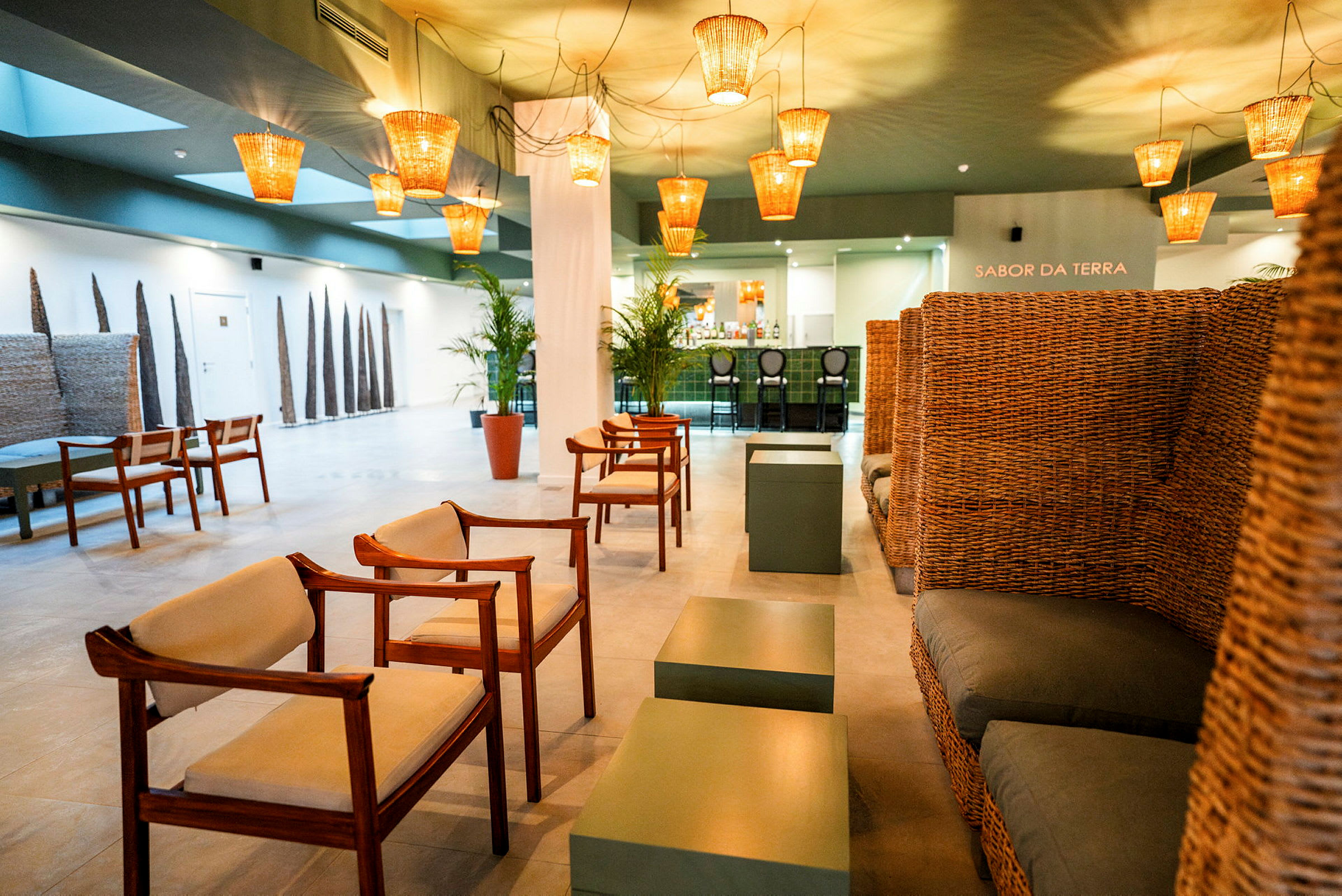 Hotellin lounge, jossa on puutuolit, rottinkipunosohvat, vihreitä pöytiä ja lämpimät kattovalaisimet. (Tekoälyn luoma teksti)