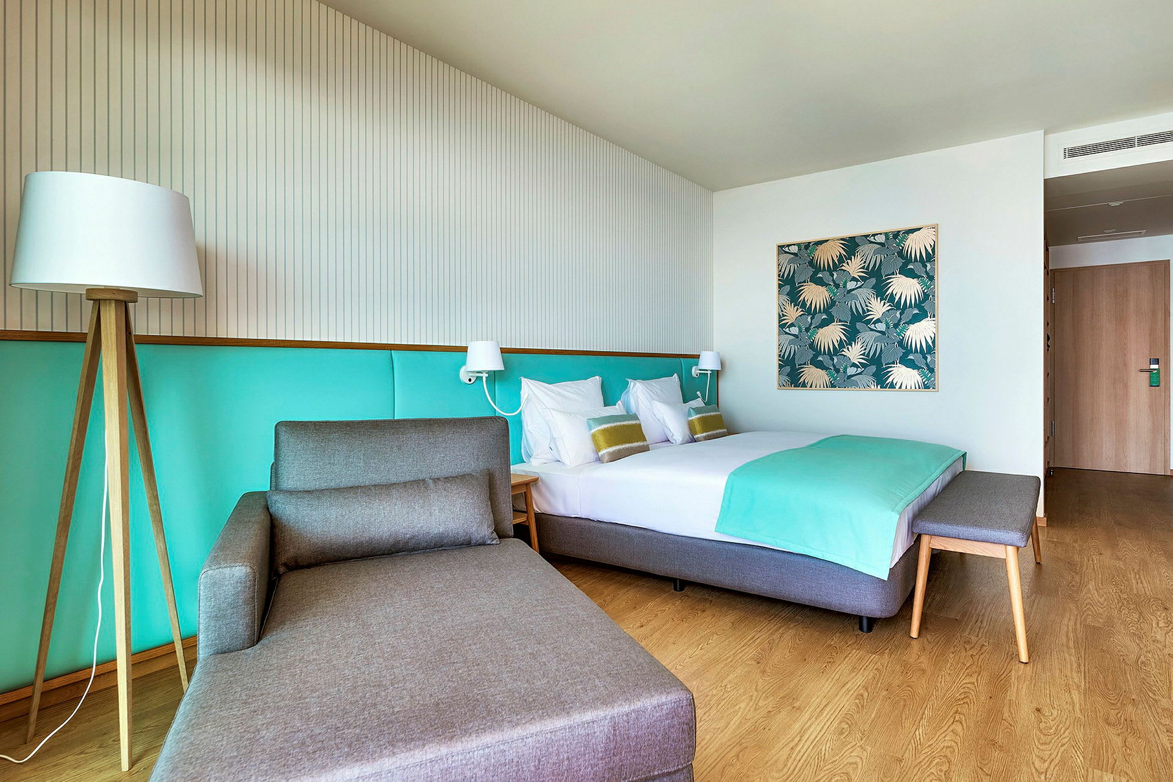 Hotellihuone, jossa on sänky, istuin ja vaalea sisustus. (Tekoälyn luoma teksti)
