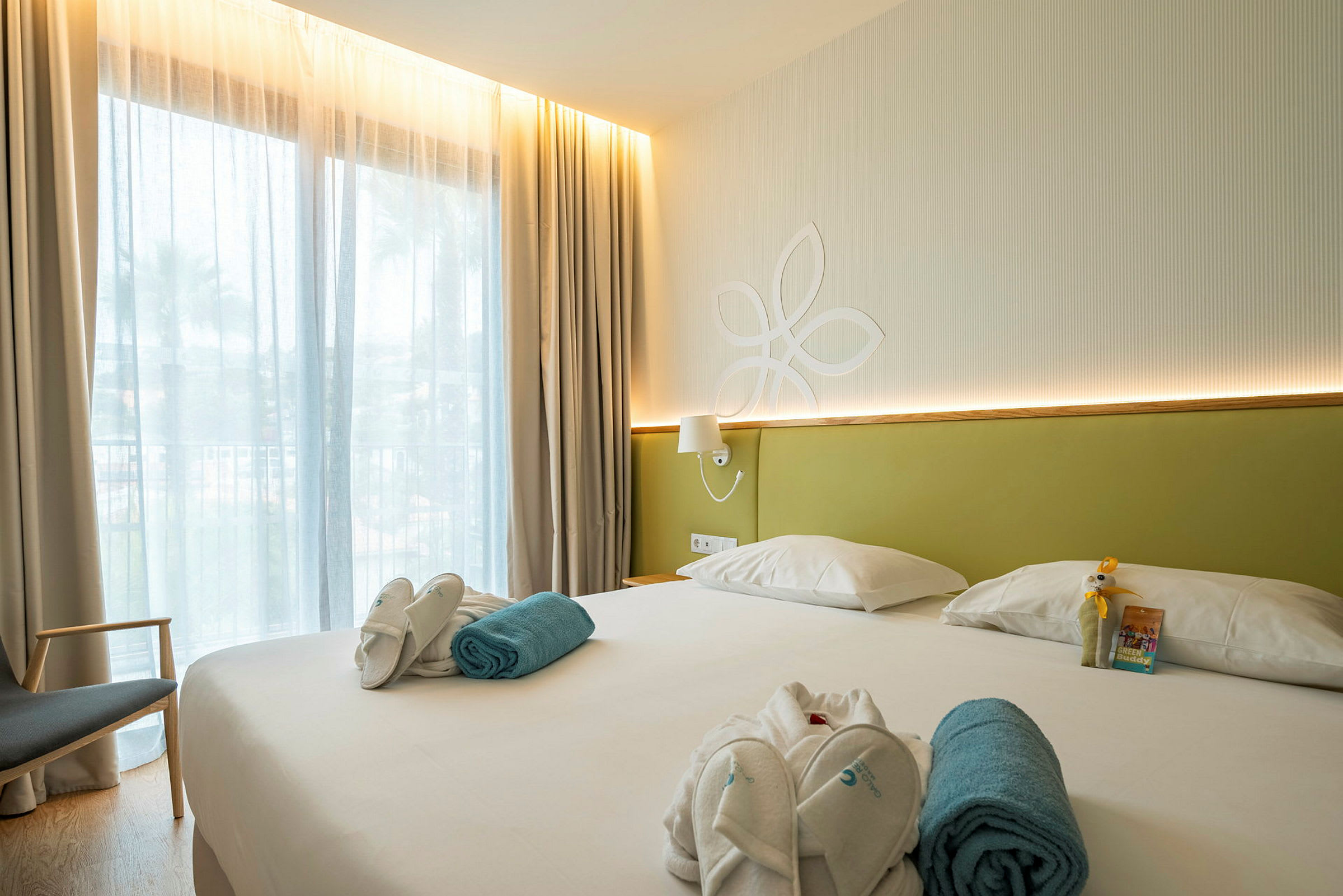 Hotellihuone, jossa on suuri sänky, vaaleaa sisustusta ja ikkuna ohuilla verhoilla. (Tekoälyn luoma teksti)