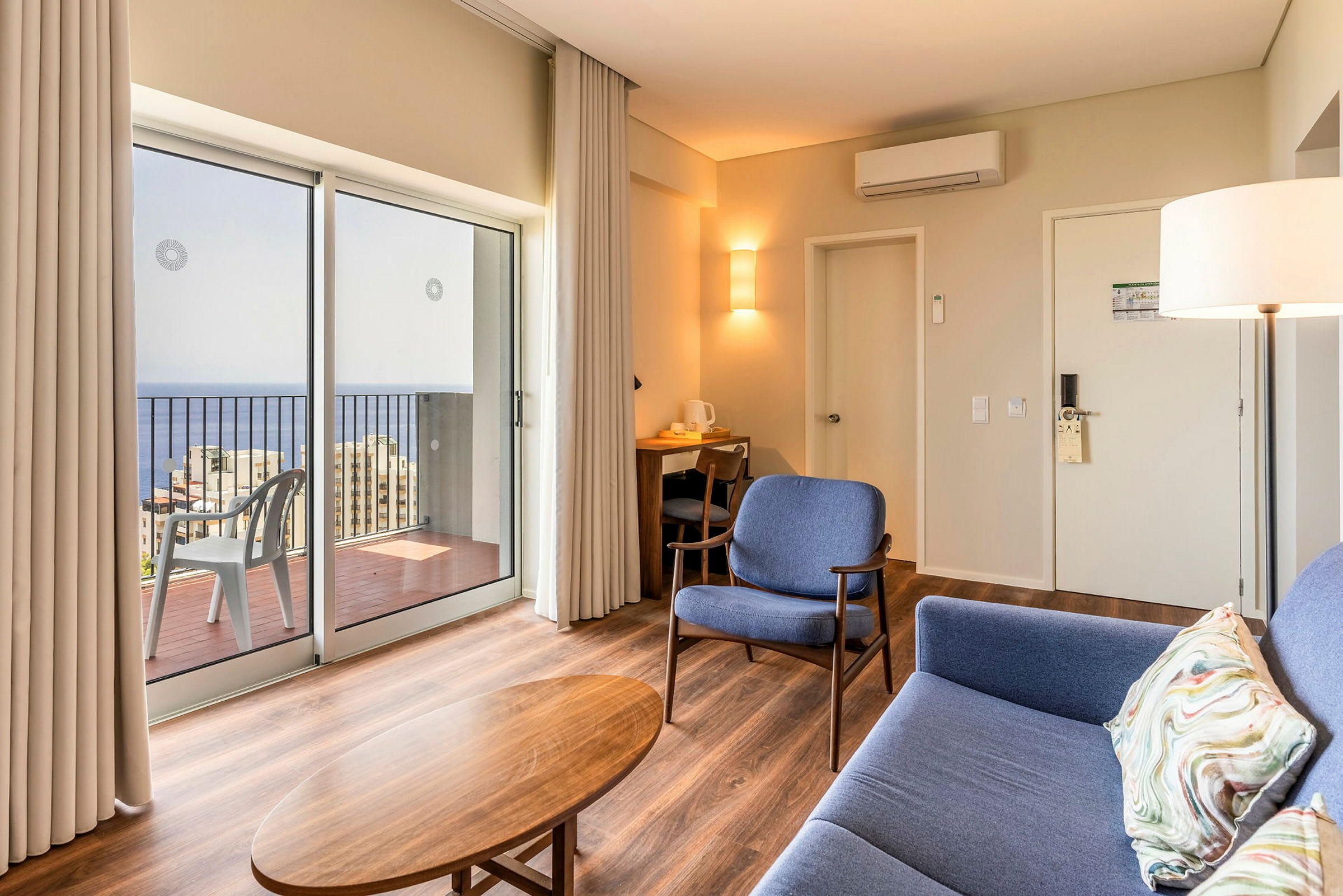 Moderni hotellihuone, jossa istuinpaikkoja ja näkymä merelle suurten ikkunoiden läpi. (Tekoälyn luoma teksti)