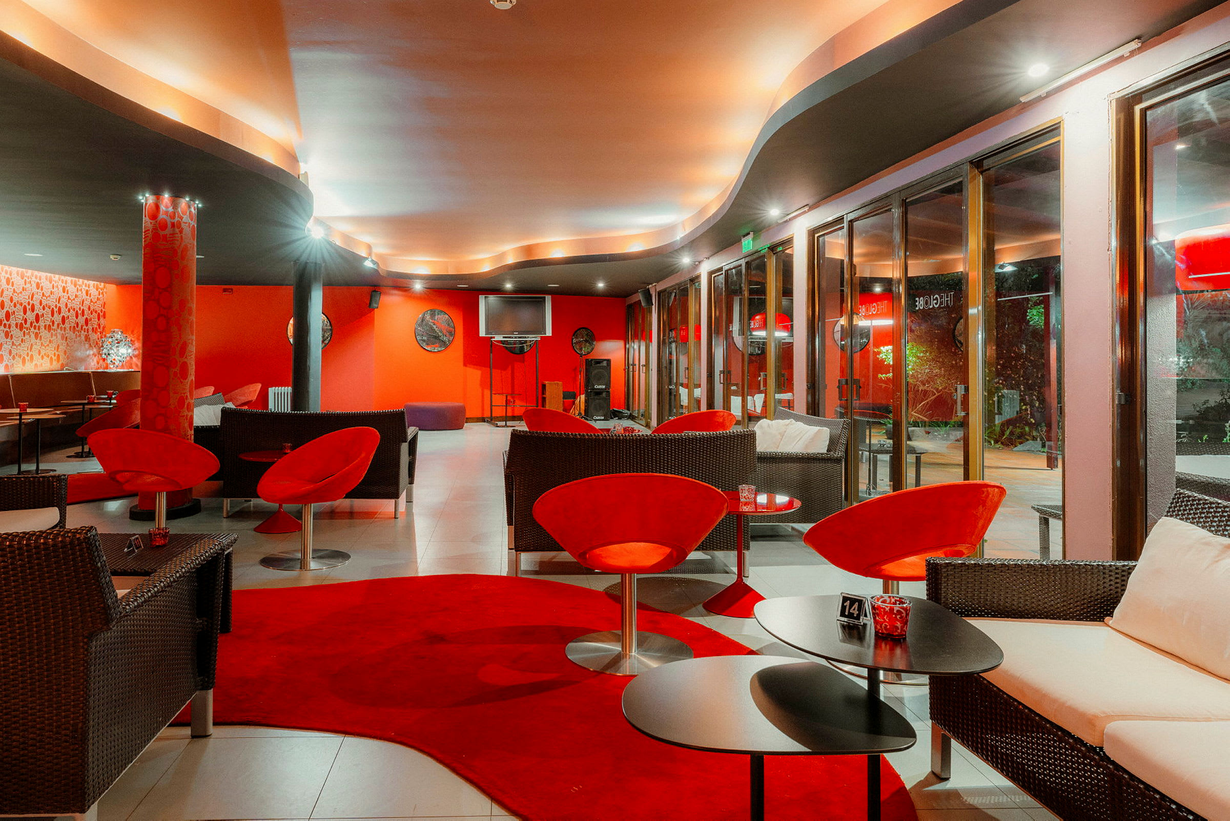Tyylikkäästi sisustettu lounge, jossa on punaisia ja tummia huonekaluja, pehmeä valaistus ja suuret ikkunat. (Tekoälyn luoma teksti)