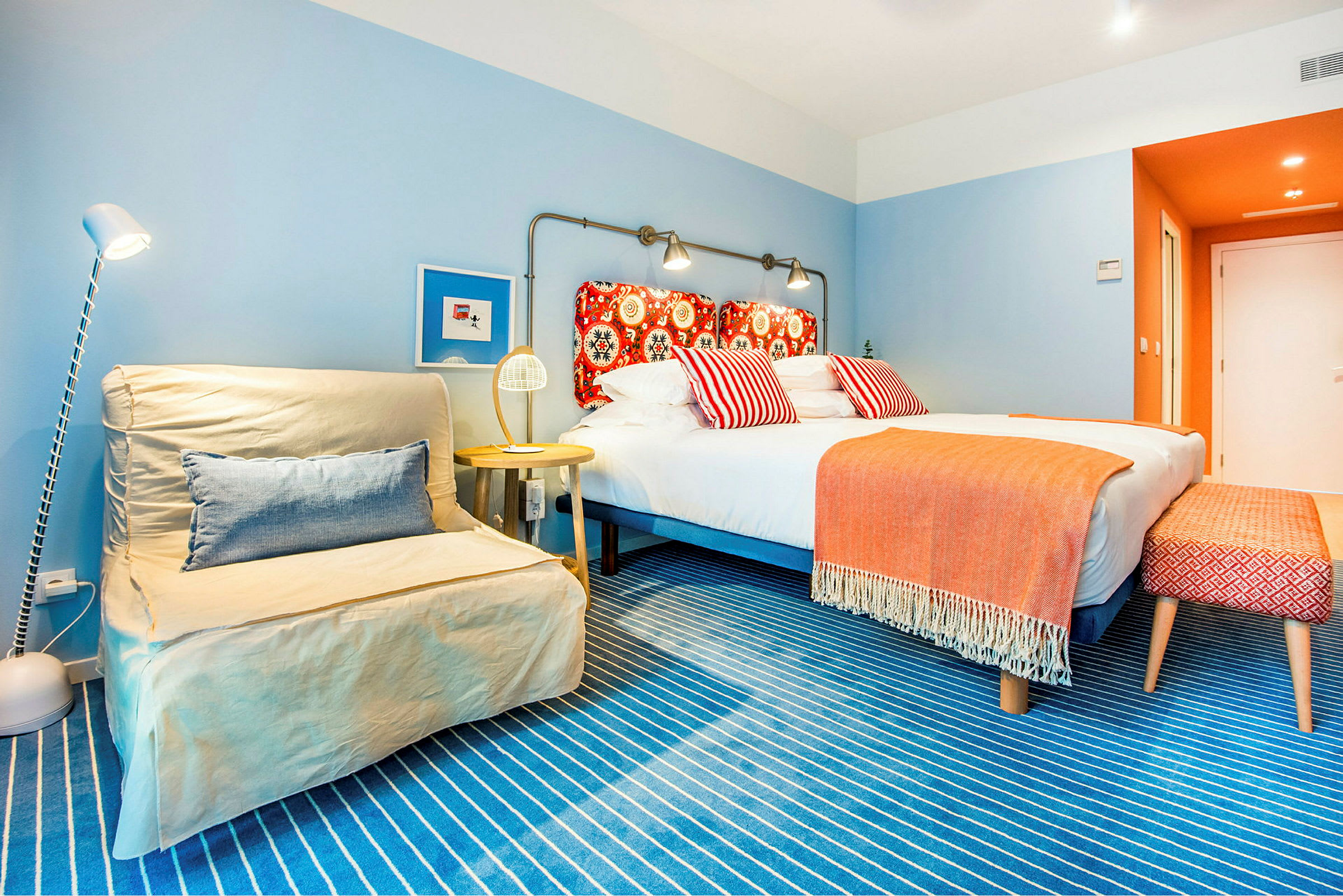 Värikäs hotellihuone, jossa on parisänky ja koristeellisia tyynyjä. (Tekoälyn luoma teksti)