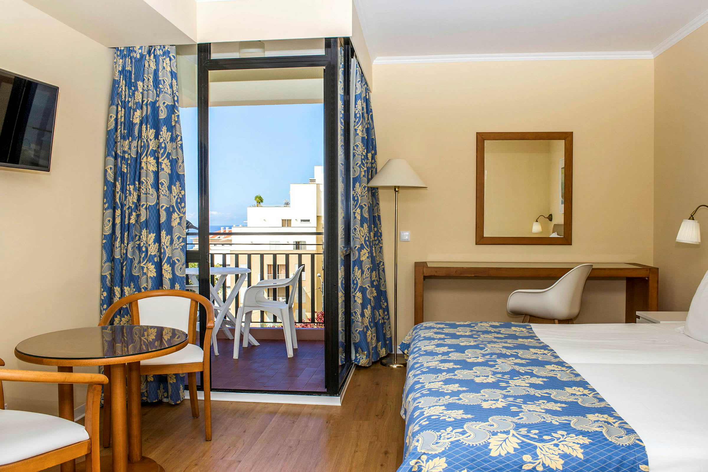 Hotellihuone, jossa vuode, pöytä ja kaksi tuolia sekä parveke näkymillä. (Tekoälyn luoma teksti)