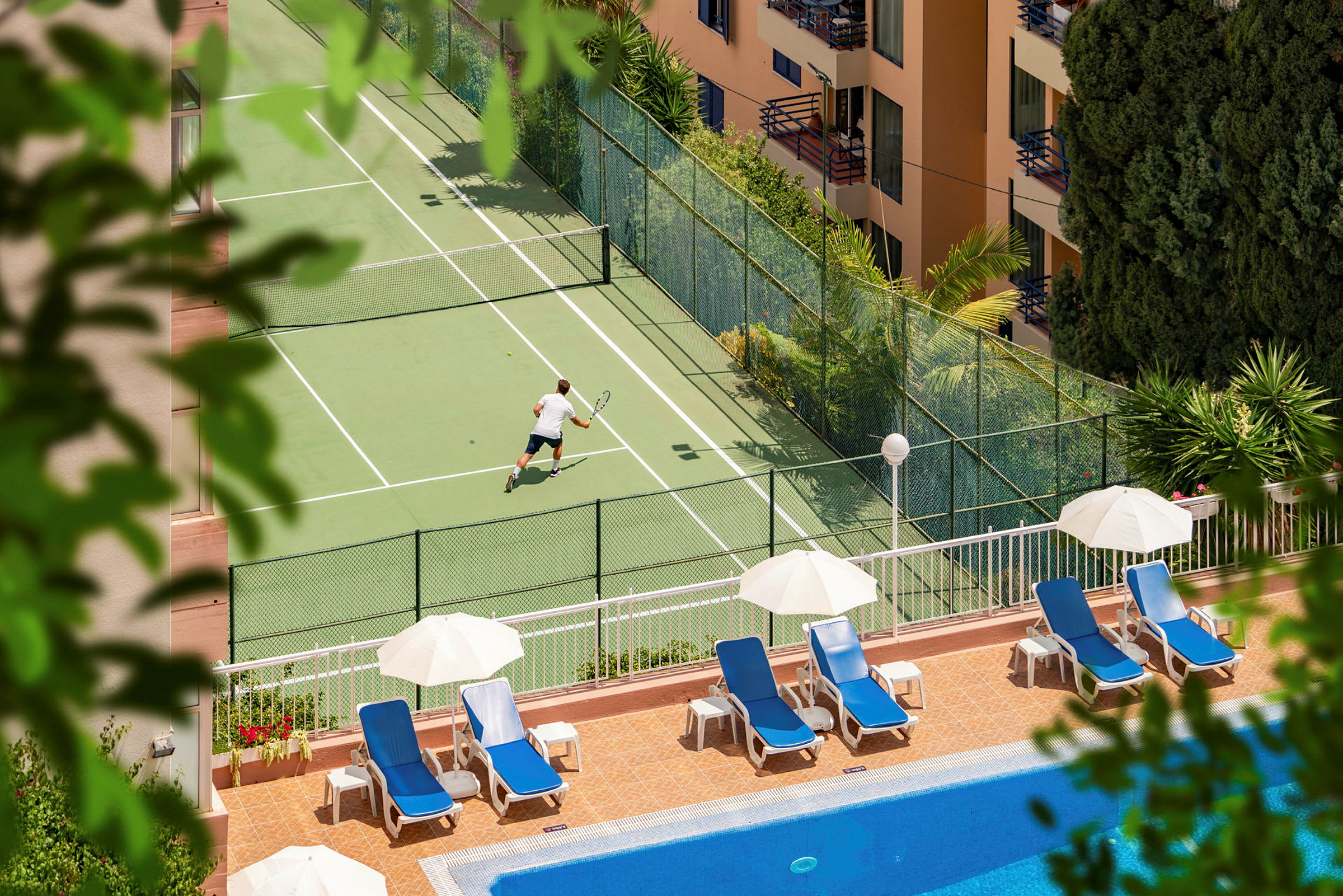 Henkilö pelaa tennistä tennis-kentällä lähellä allasta, jossa on aurinkotuoleja ja -varjoja. (Tekoälyn luoma teksti)