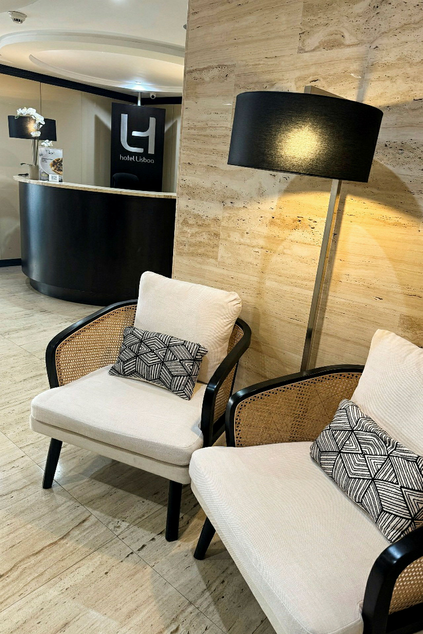 Kaksi tuolia, joissa koristeelliset tyynyt, lattiavalo ja vastaanottotiski, jossa kyltti tekstillä "Hotel Lisboa". (Tekoälyn luoma teksti)