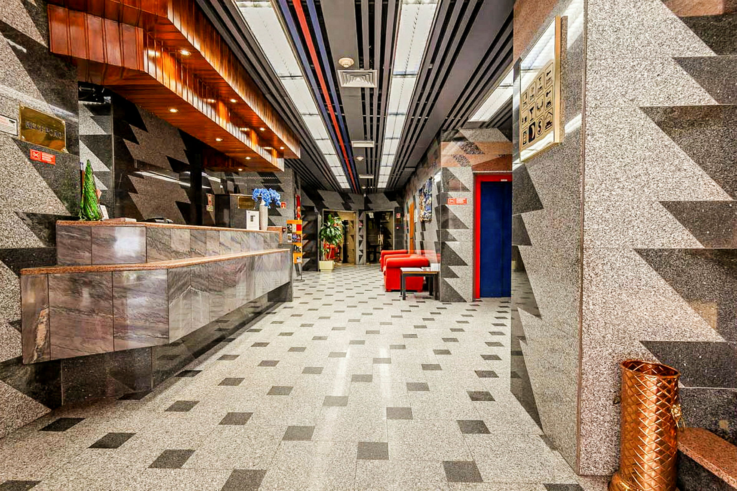 Hotellin aula marmorisella sisustuksella, vastaanottoalueella ja punaisilla istuinkalusteilla. (Tekoälyn luoma teksti)