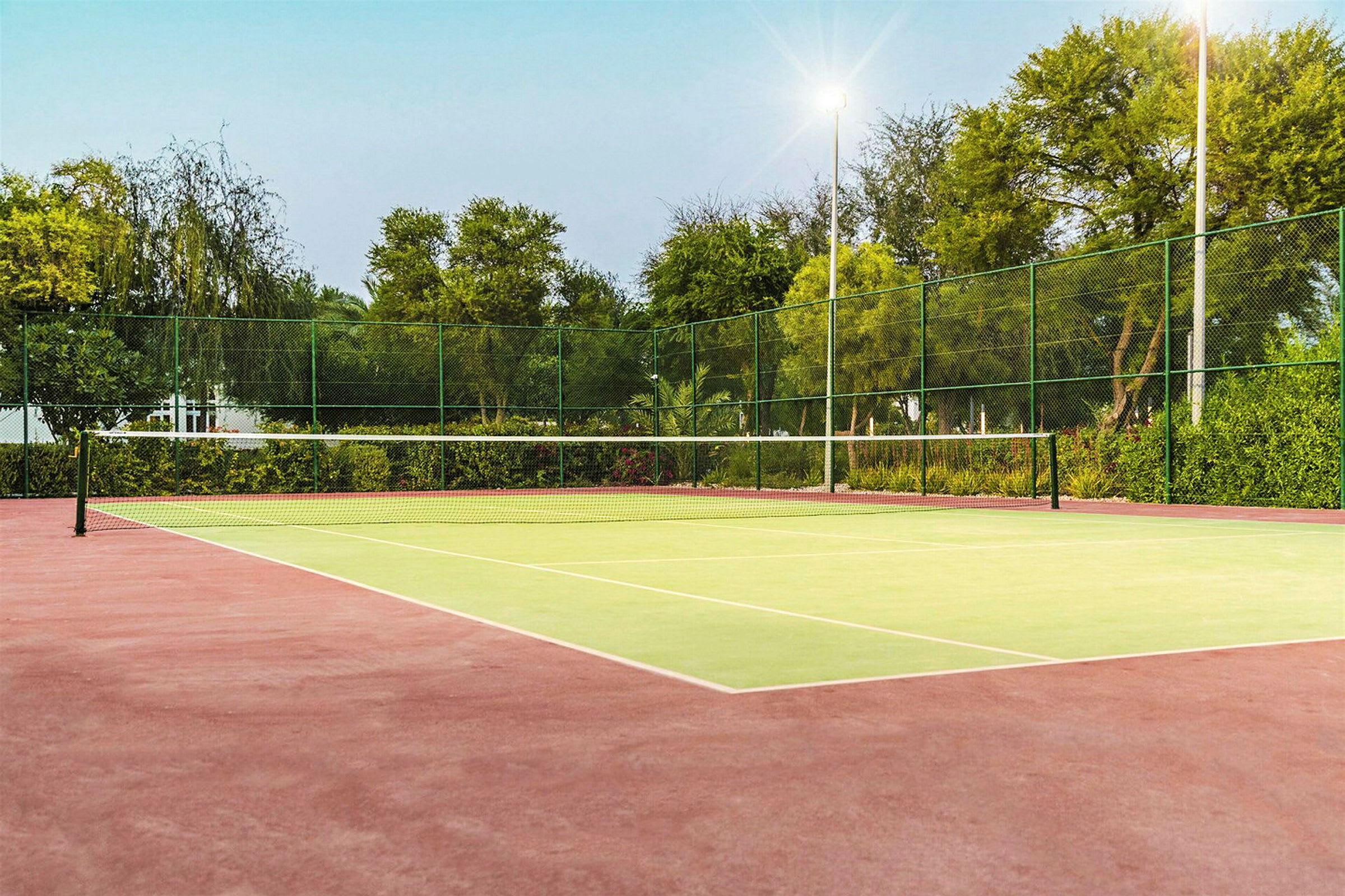Tyhjä tenniskenttä, jossa verkko ja ympärillä vihreää kasvillisuutta. (Tekoälyn luoma teksti)
