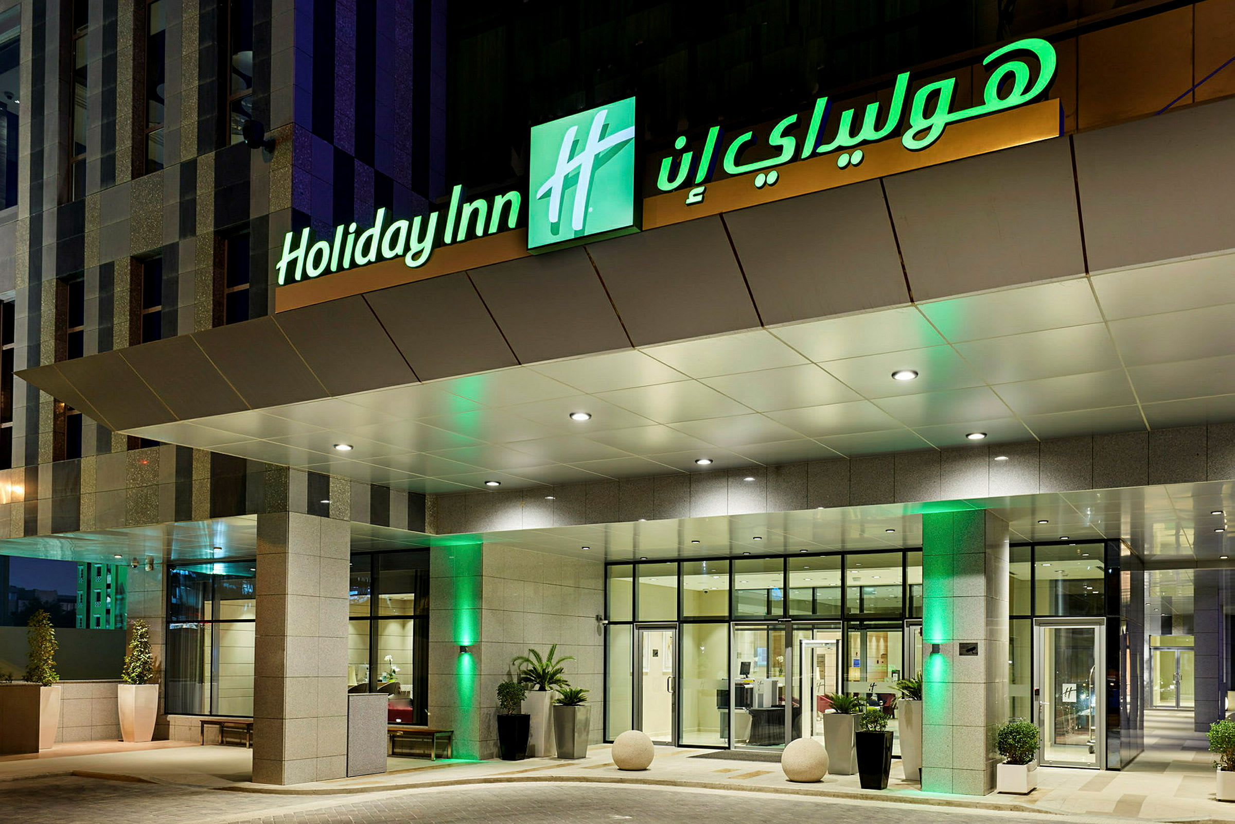 Hotellin sisäänkäynti, jossa valaistu 'Holiday Inn' -kyltti. (Tekoälyn luoma teksti)