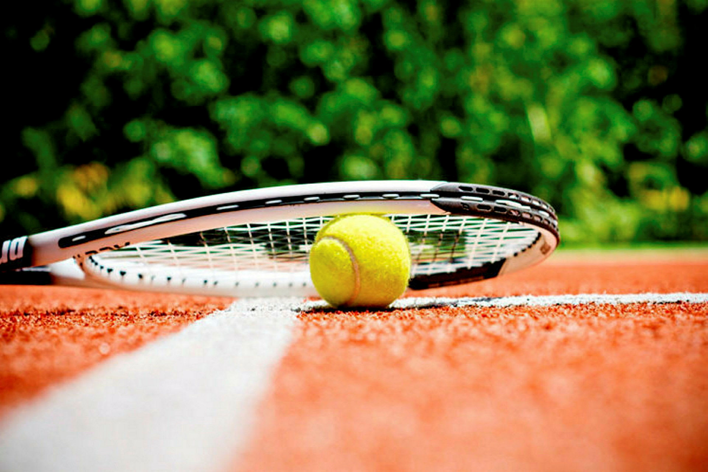 Tennispallo ja maila ovat punaisella tenniskentällä lähellä valkoista viivaa. (Tekoälyn luoma teksti)