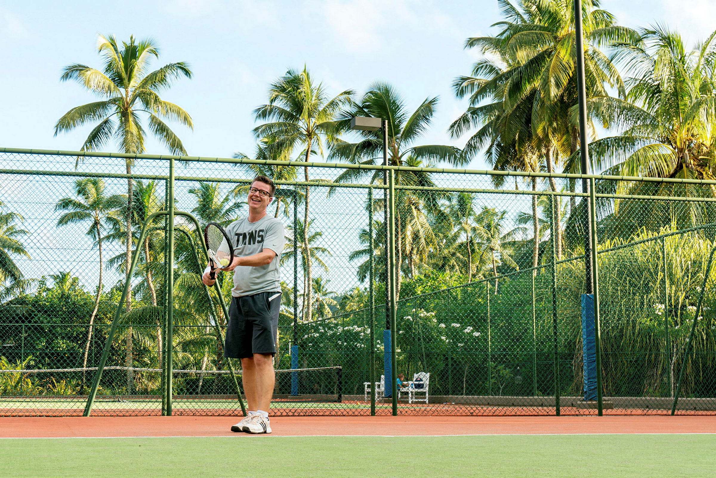 Henkilö pelaa tennistä kentällä, jota ympäröi vehreys ja palmut. (Tekoälyn luoma teksti)