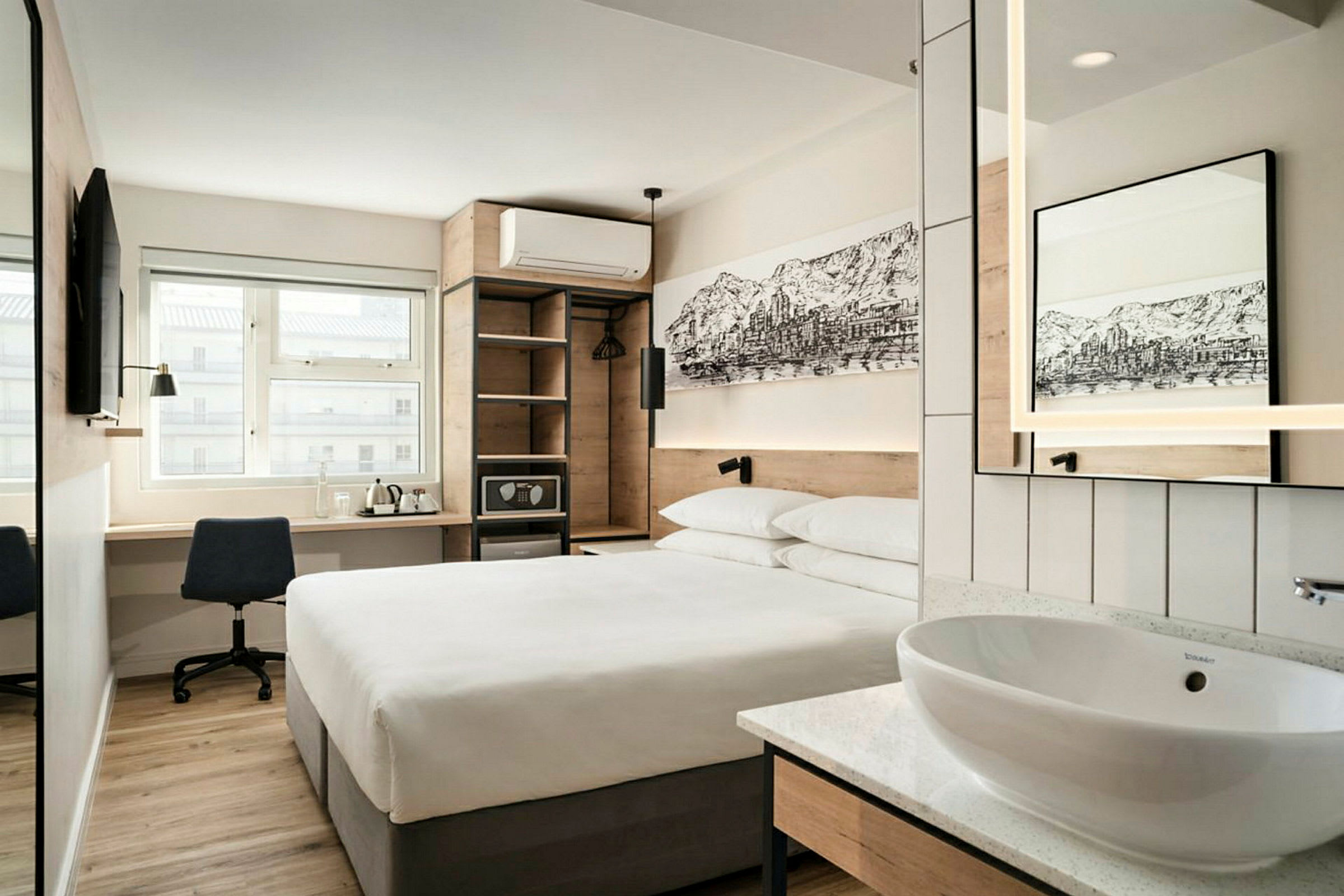 Moderni hotellihuone, jossa on parivuode, kirjoituspöytä ja tuoli, seinälle asennettu televisio sekä avonaulakko ja pieni pesuallas peileineen. (Tekoälyn luoma teksti)